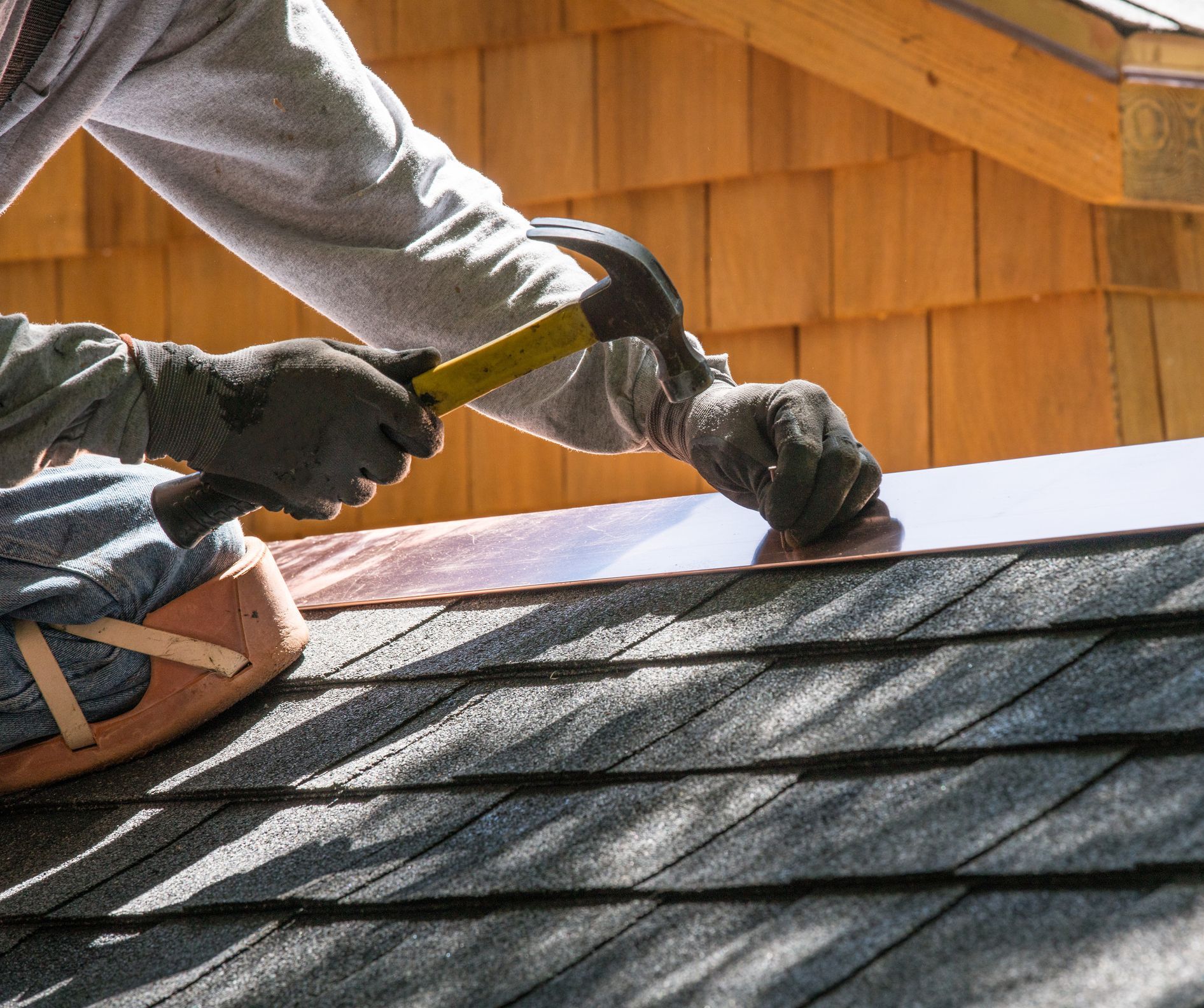 Close-up of a roofing contractor installing a new asphalt roof with a hammer.