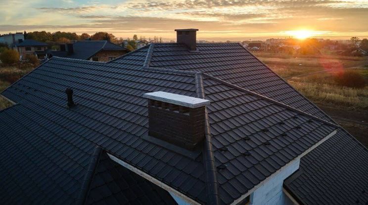 An aerial view of a roof with a chimney and a sunset in the background.