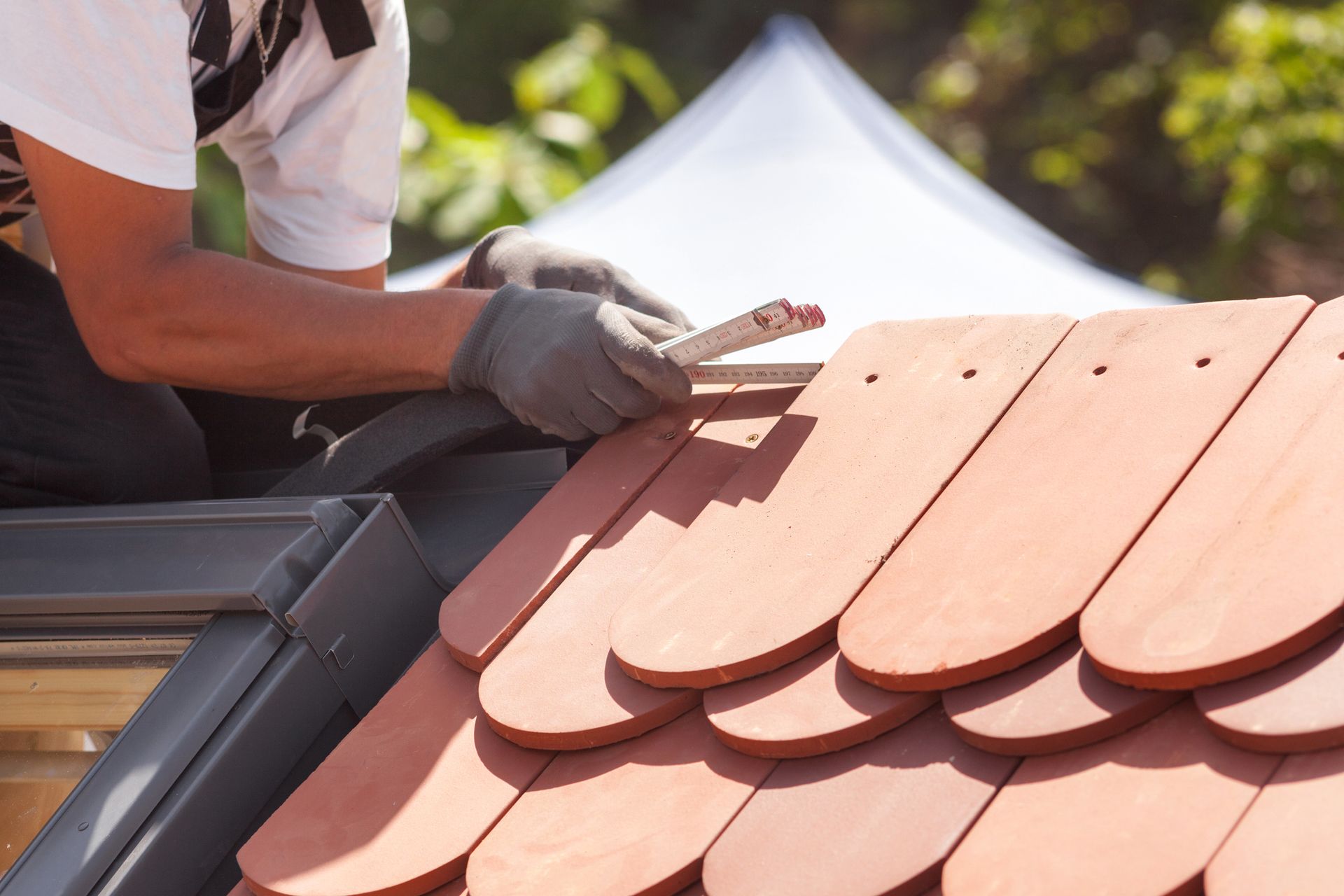 Roofer measuring clay shingles during roof installation on a sunny day.