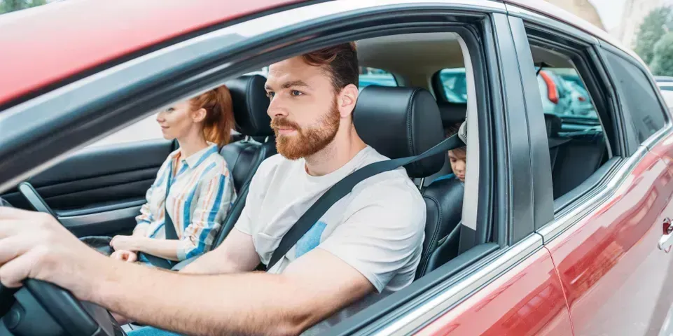 A man driving a red car with passengers sitting in the front and back seats.