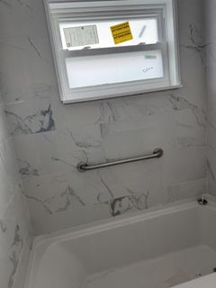 A bathtub in a bathroom with marble walls and a window.