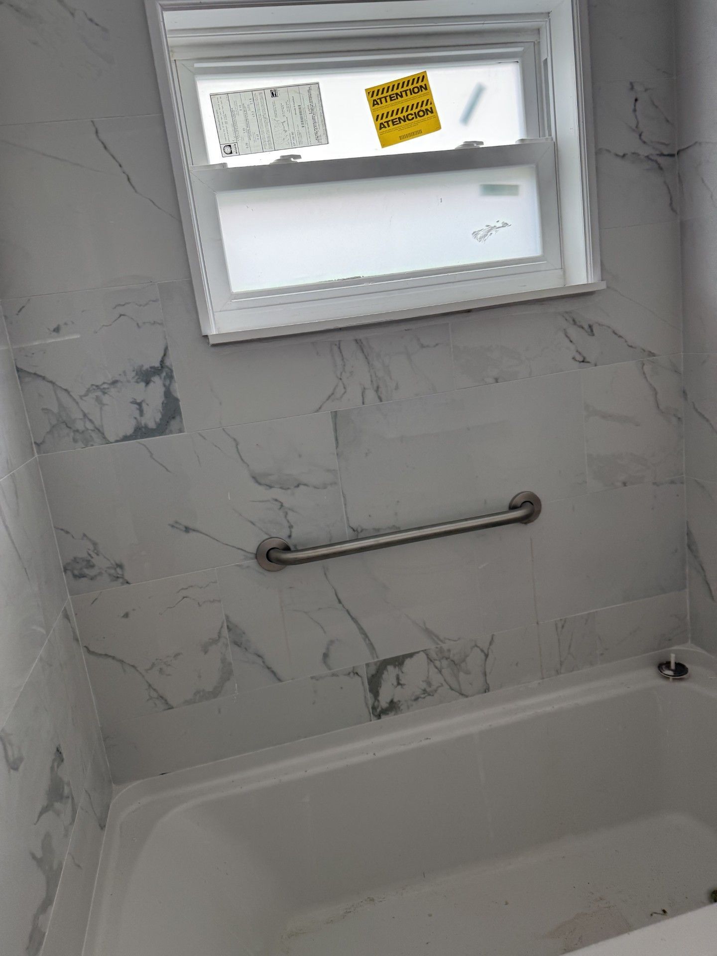 A bathtub in a bathroom with marble walls and a window.