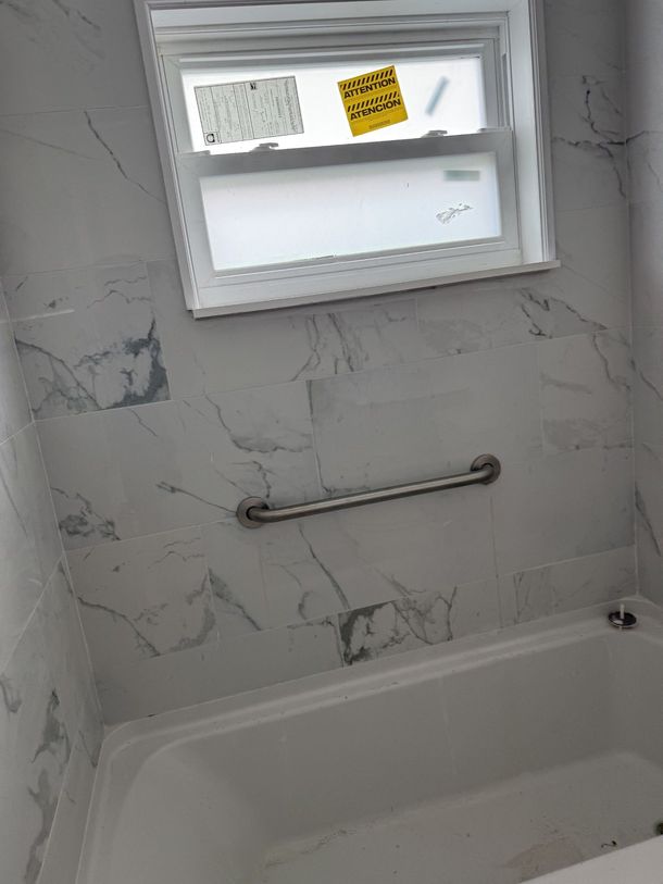 A bathtub in a bathroom with marble walls and a window.