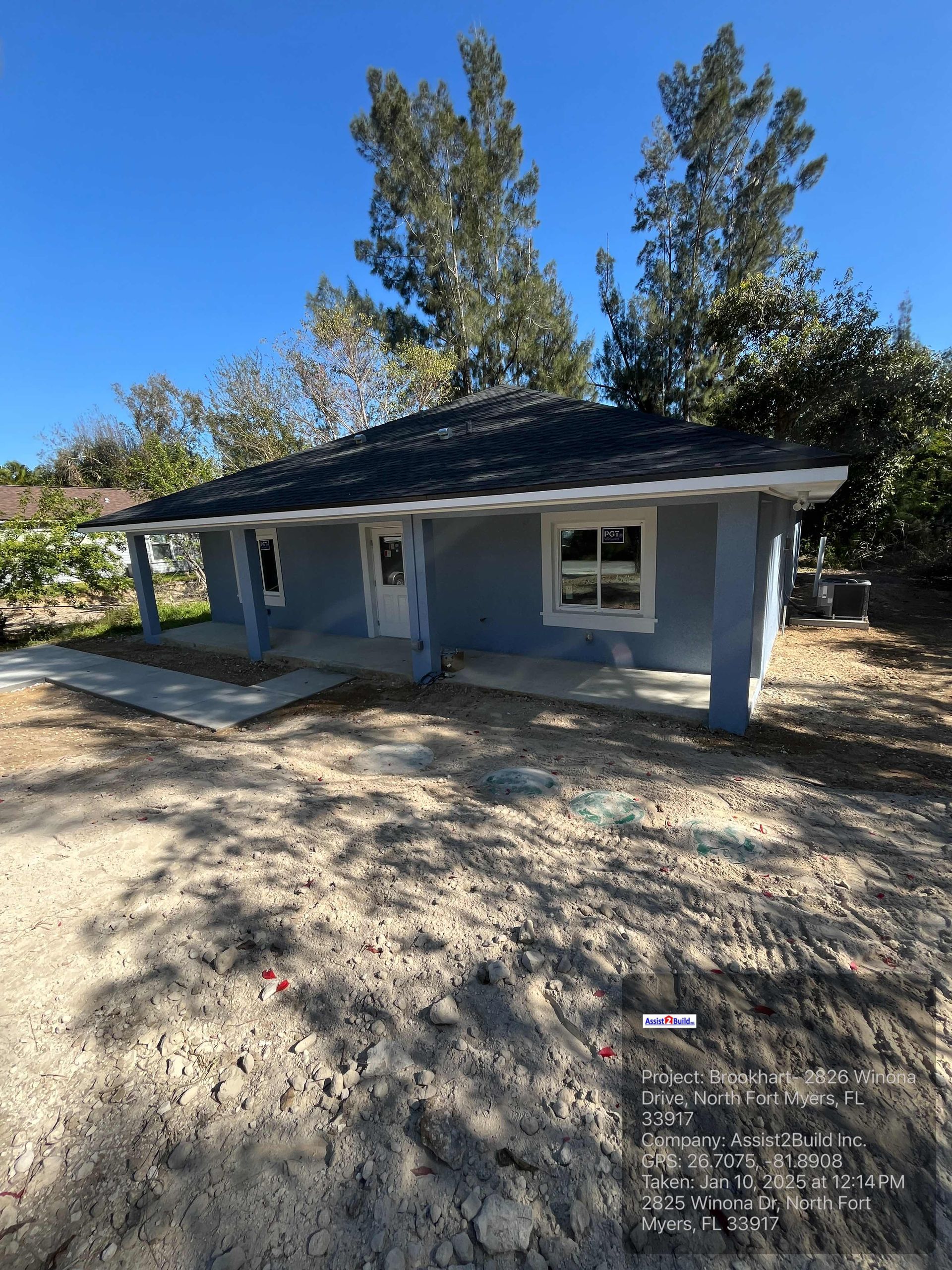 A small blue house with a porch and trees in the background.