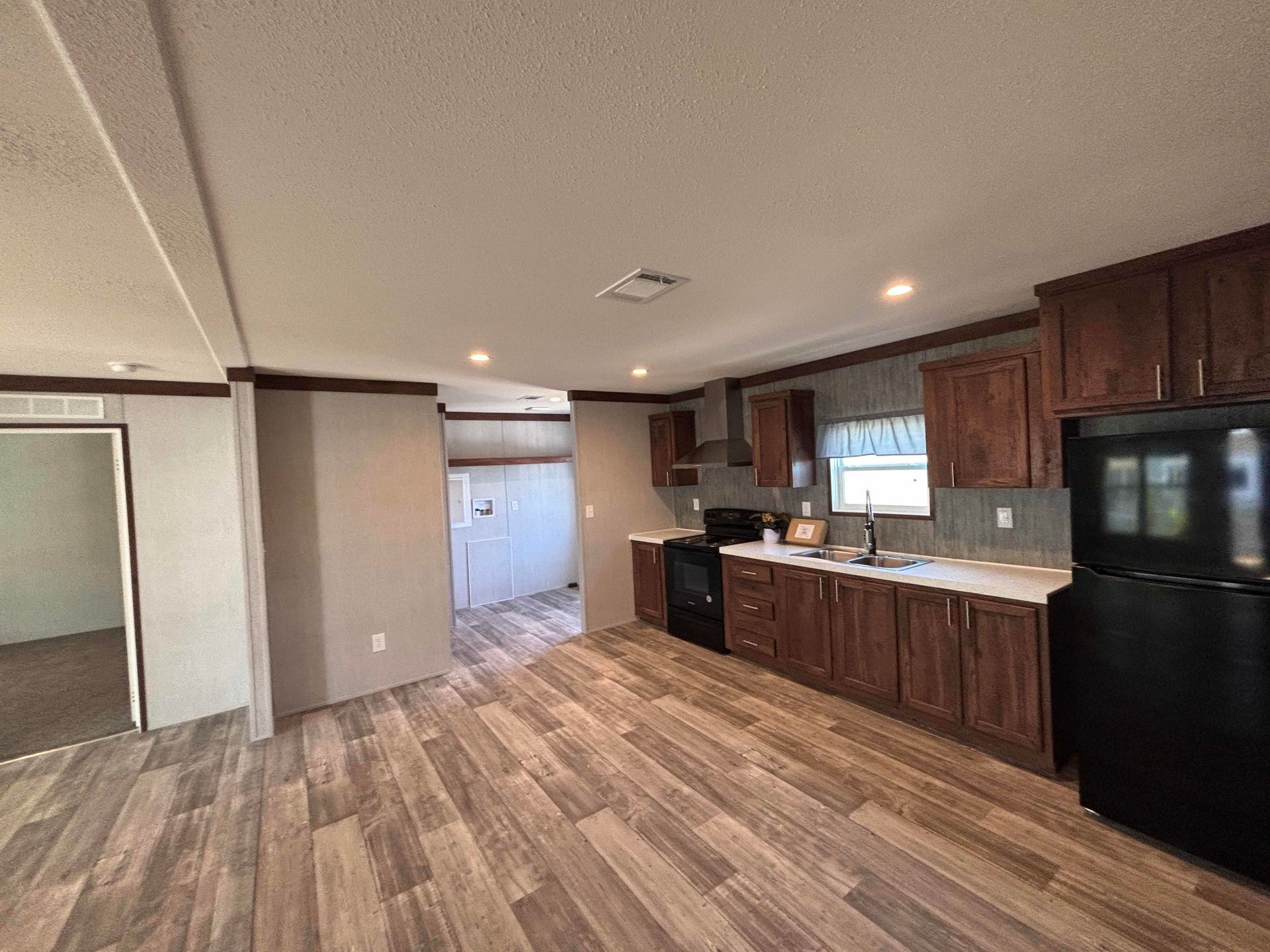 A kitchen in a mobile home with wooden cabinets and a black refrigerator.