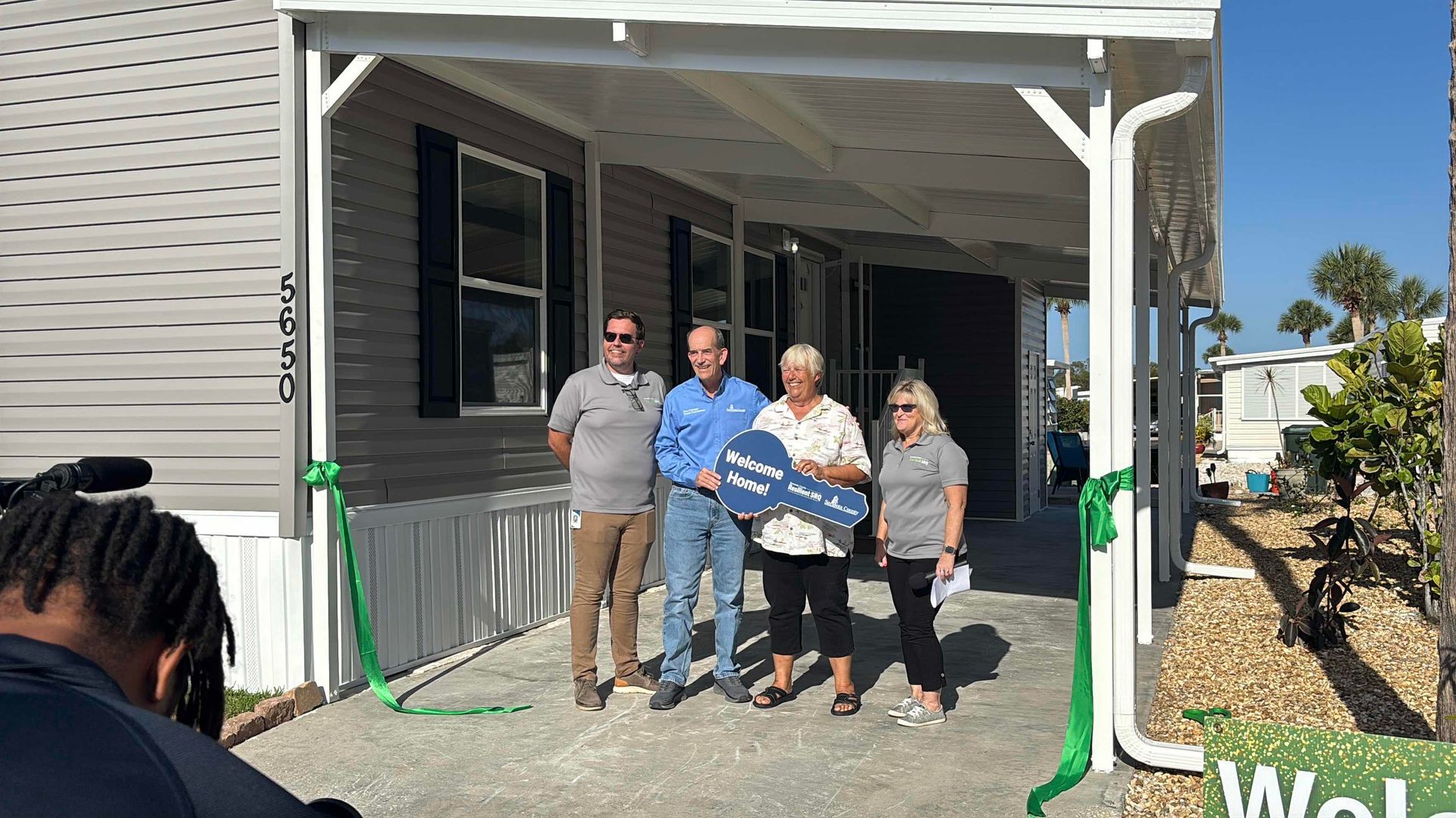 A group of people are standing in front of a mobile home holding a key.