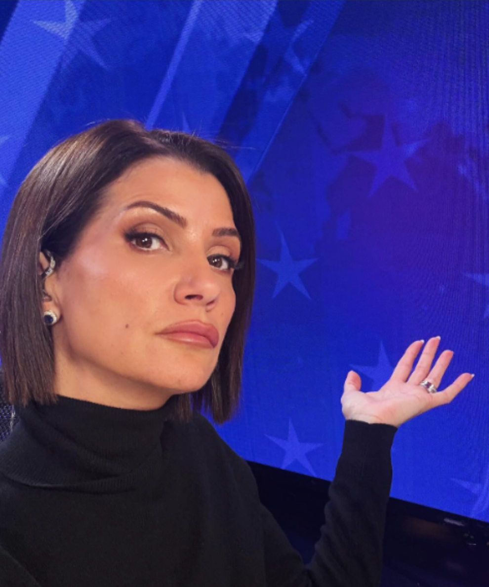 A woman in a black turtleneck holds her hand up in front of a blue background with stars