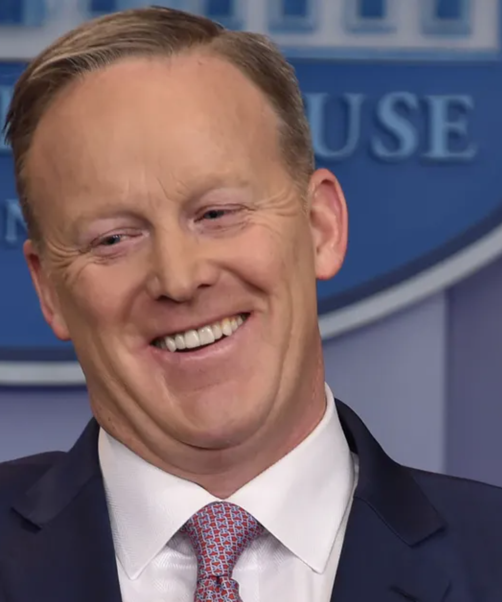 A man in a suit and tie is smiling in front of a white house logo