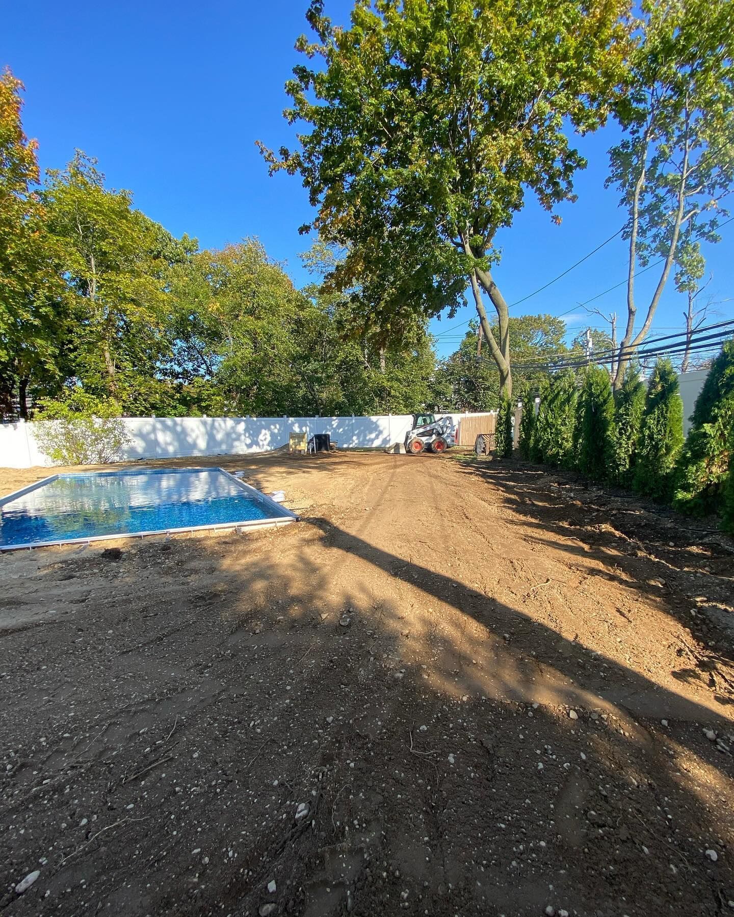A swimming pool is surrounded by trees and dirt in a backyard.