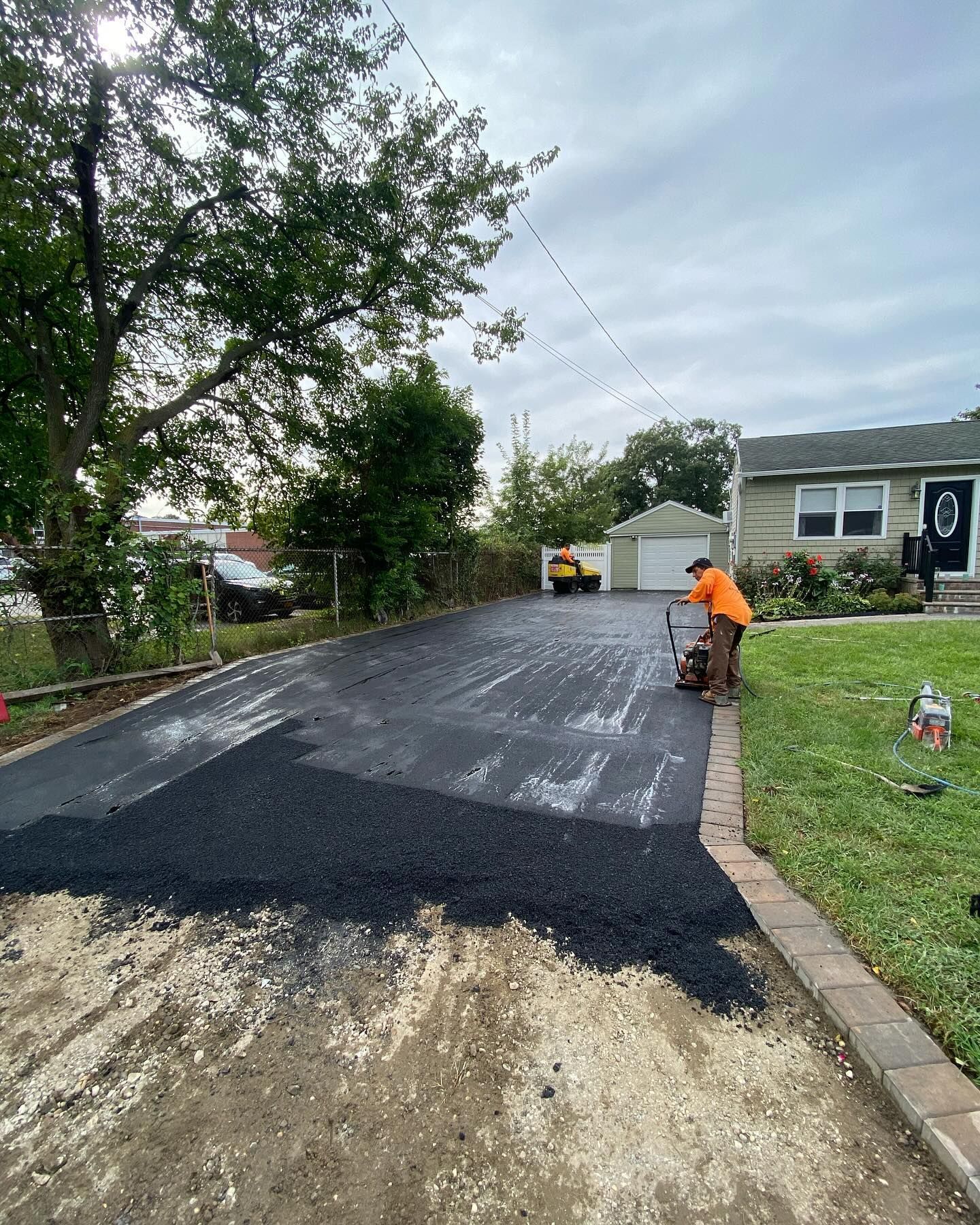 A man is paving a driveway in front of a house.