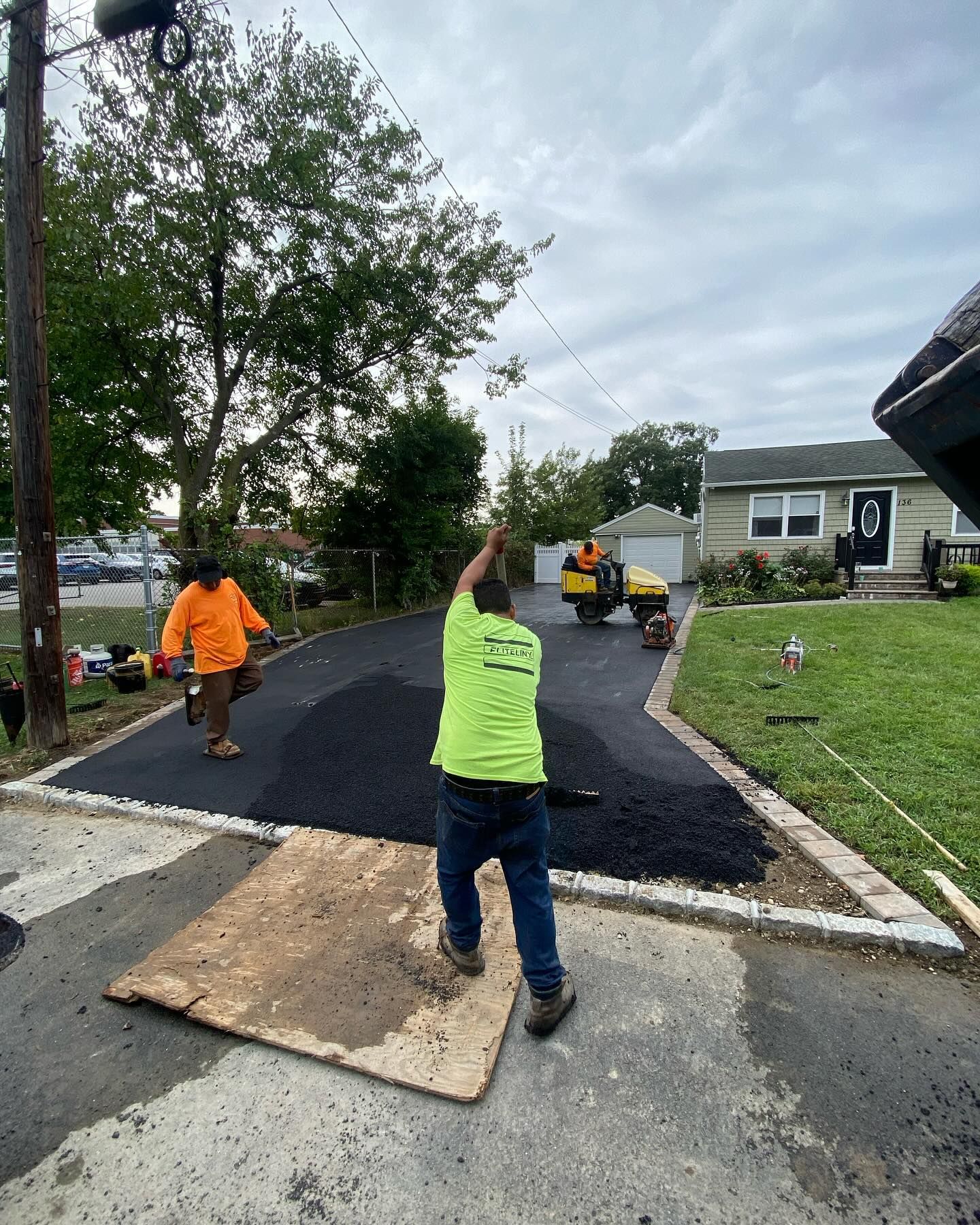 A man in a neon yellow shirt is standing on a wooden board in a driveway.