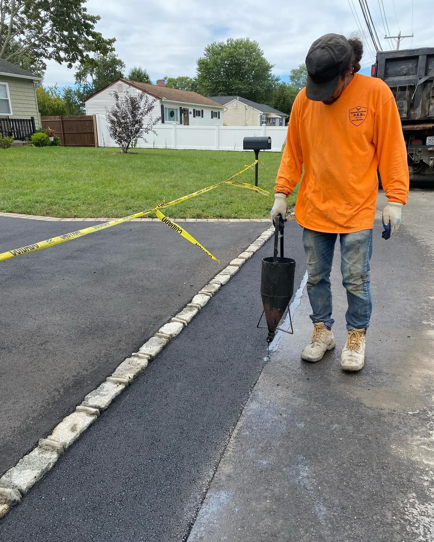 A man in an orange shirt is working on a driveway