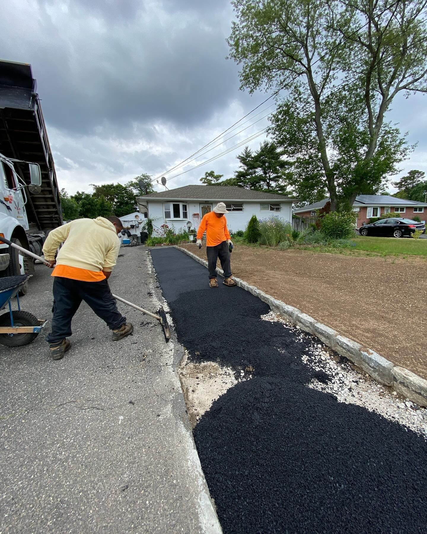 Two men are working on a driveway in front of a house.