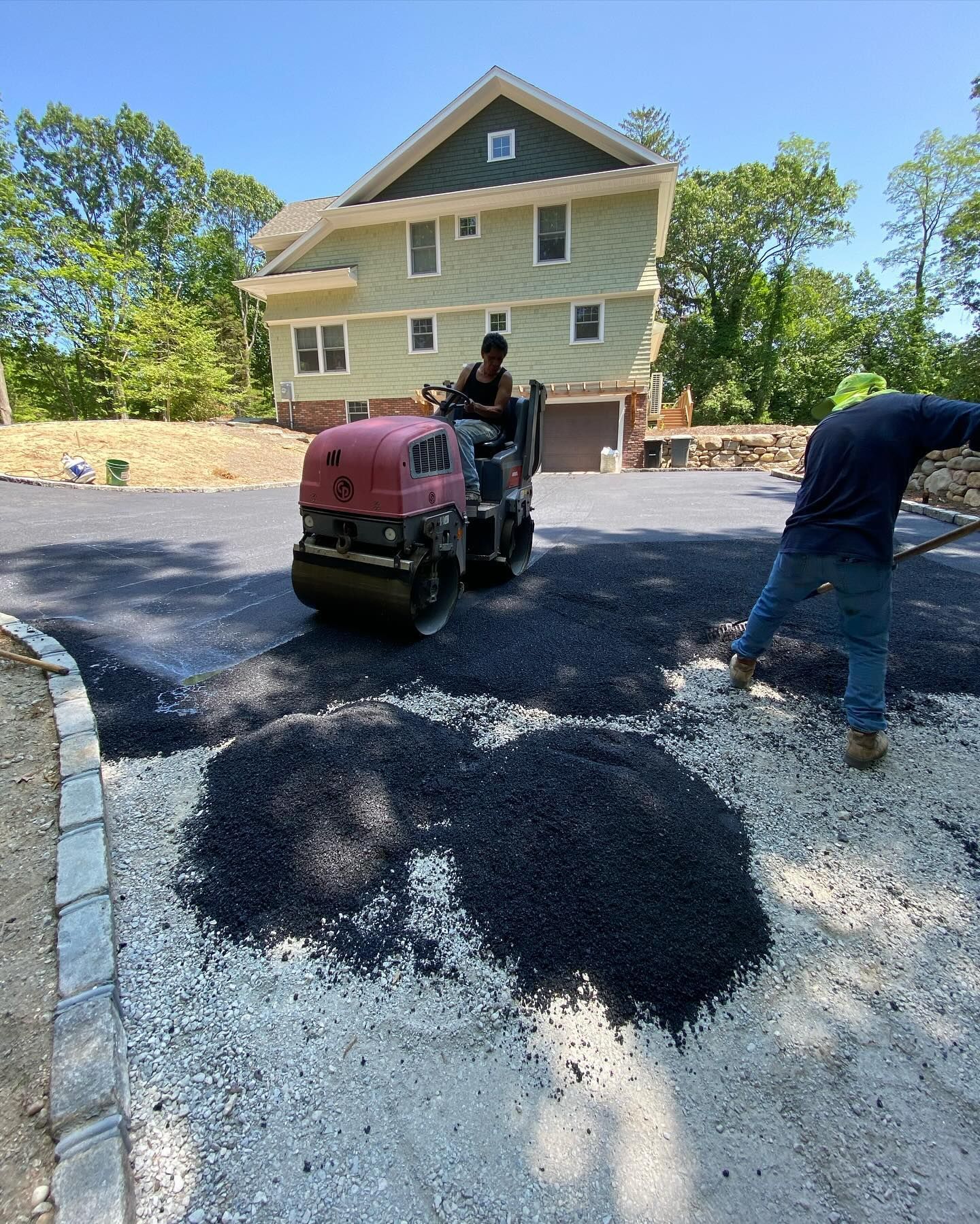 A man is driving a roller on a road in front of a house.