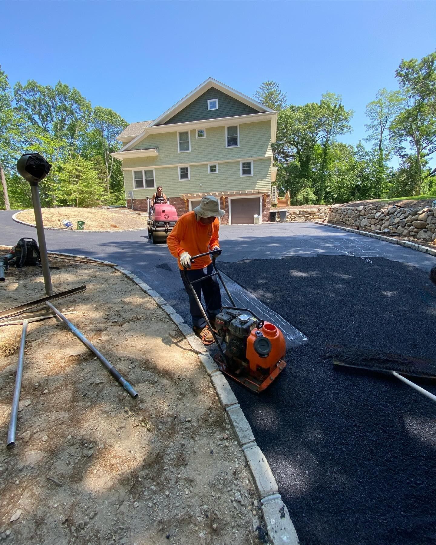 A man is laying asphalt on a driveway in front of a house.