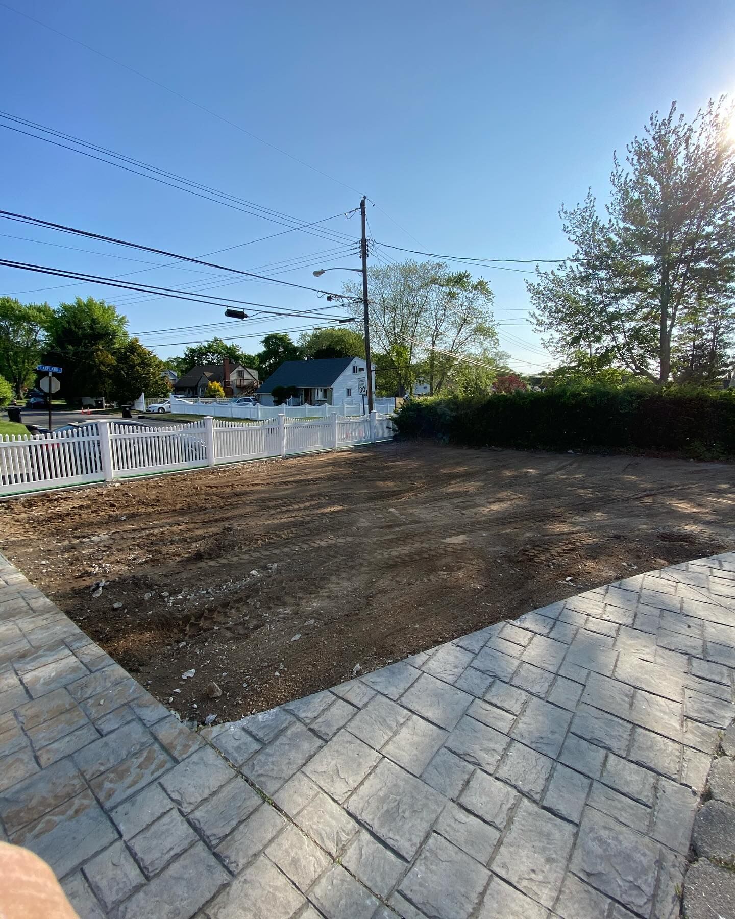 A brick walkway leading to a dirt field with a white fence in the background.