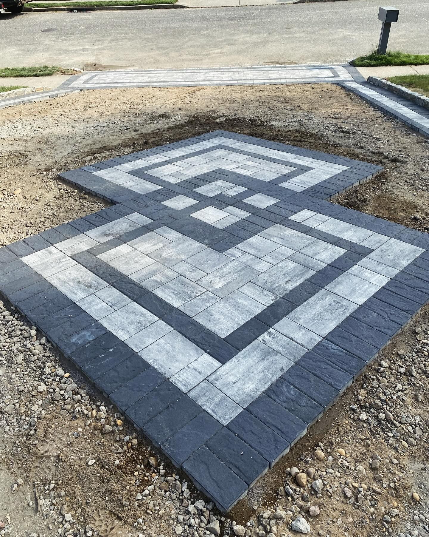 A black and white brick walkway is being built in the dirt.