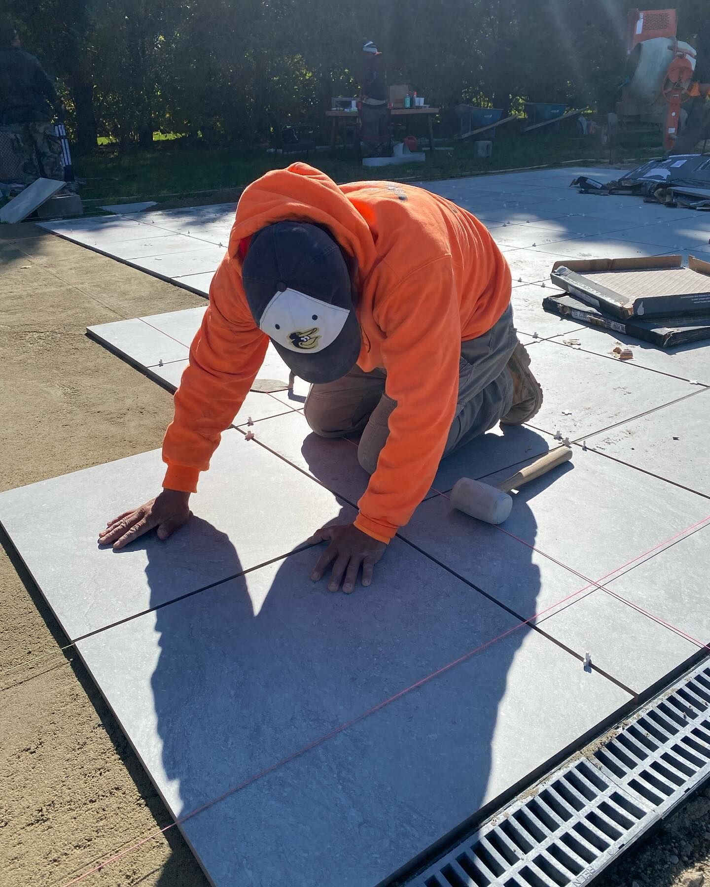 A man is kneeling on a tile floor with a hammer.