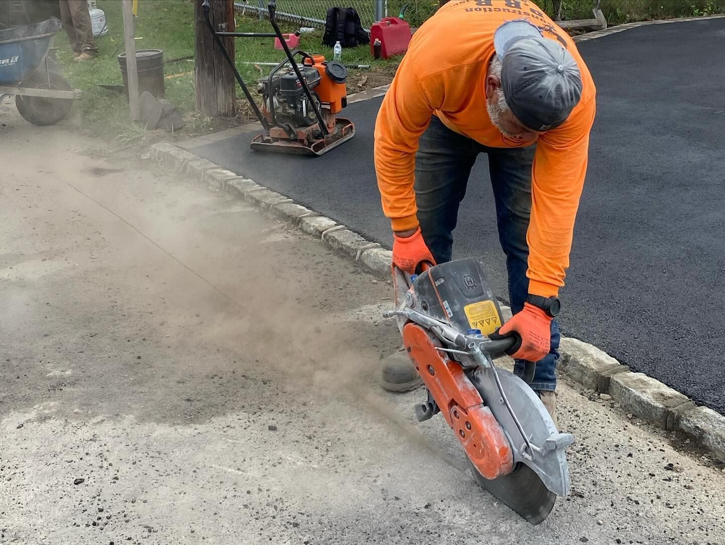 A man is using a concrete saw to cut a road.