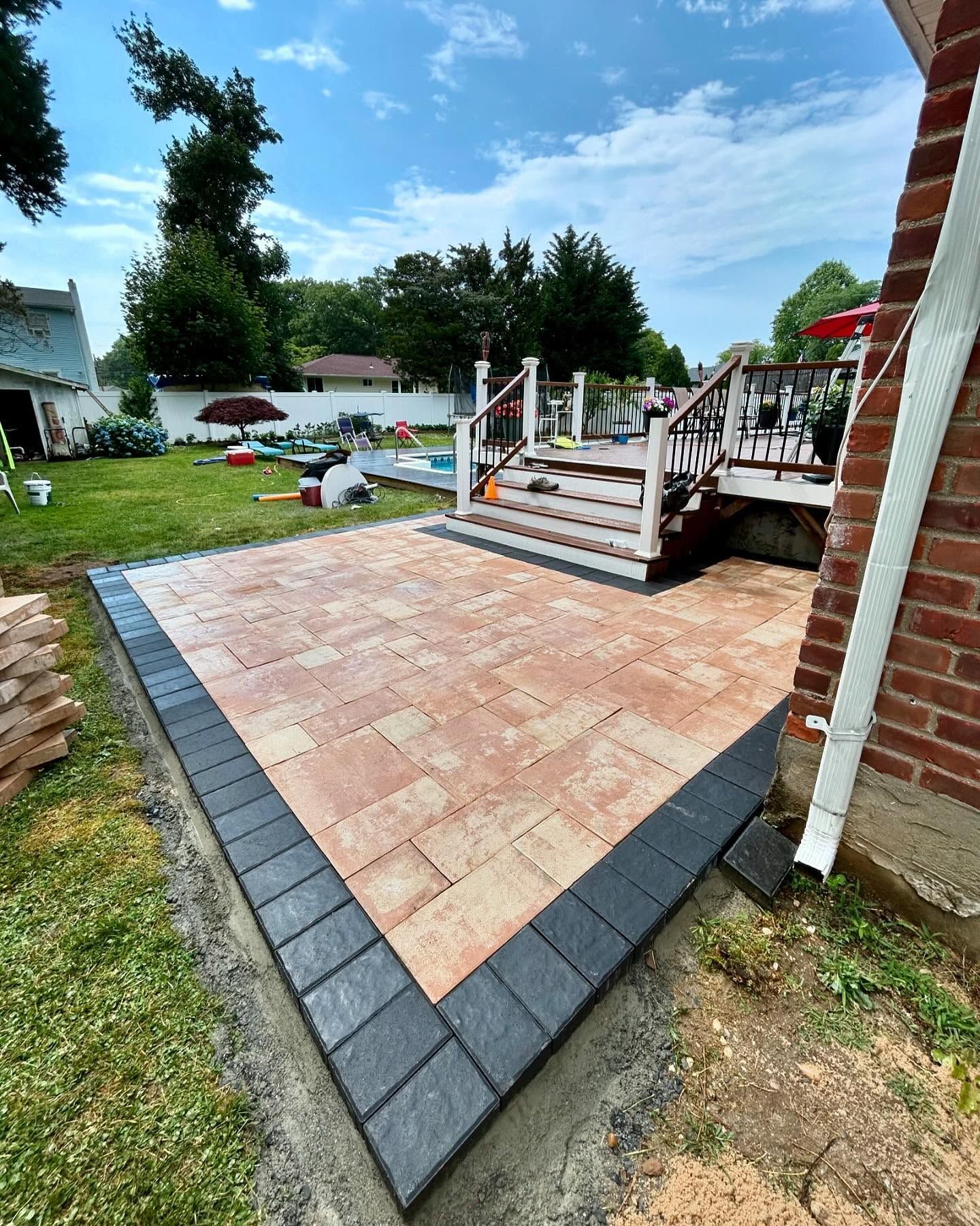 A brick patio with a black border is being built in the backyard of a house.