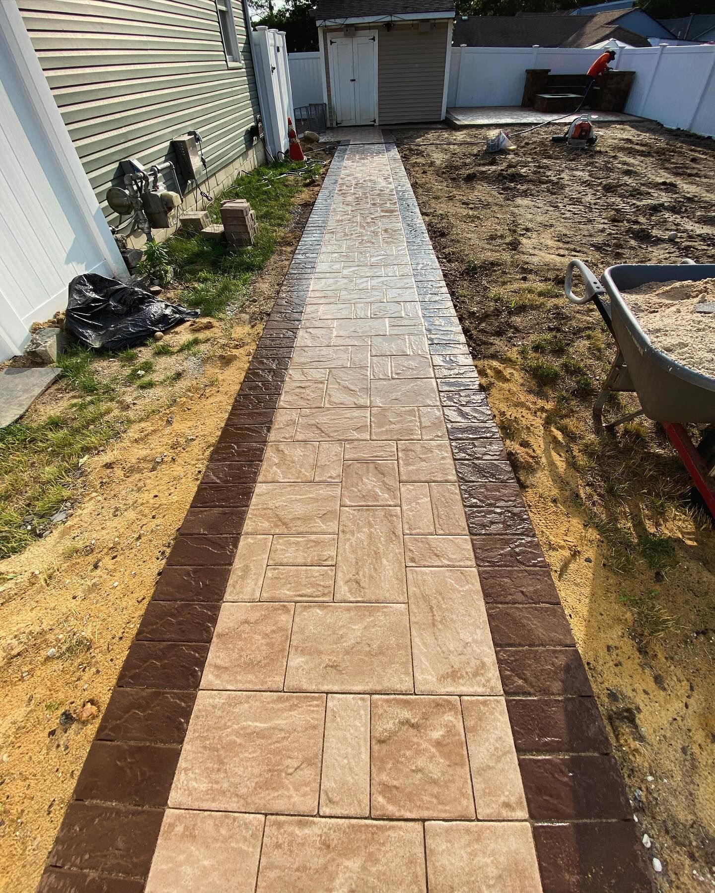 A brick walkway is being built in the backyard of a house.