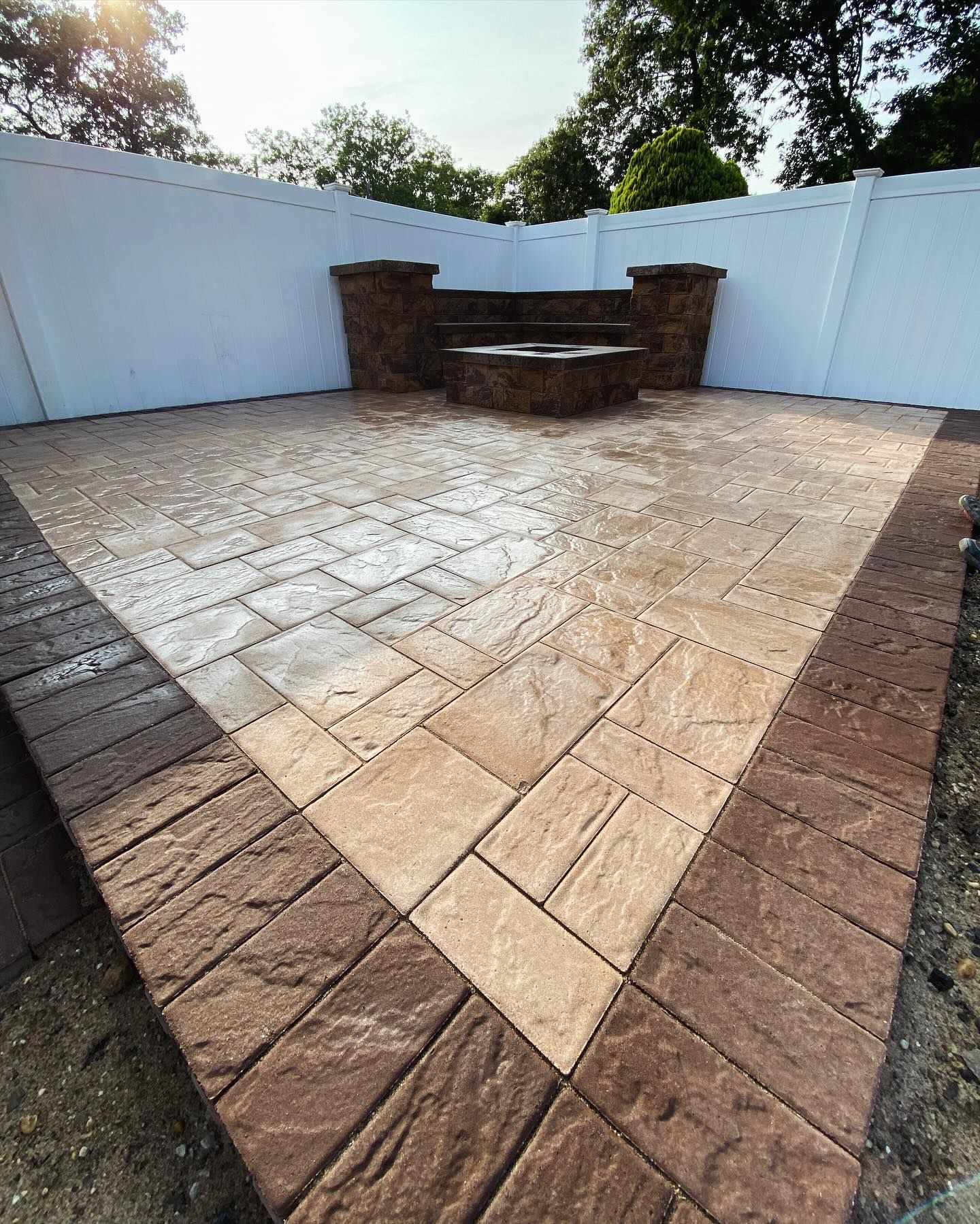 A patio with a bench and a white fence in the background.
