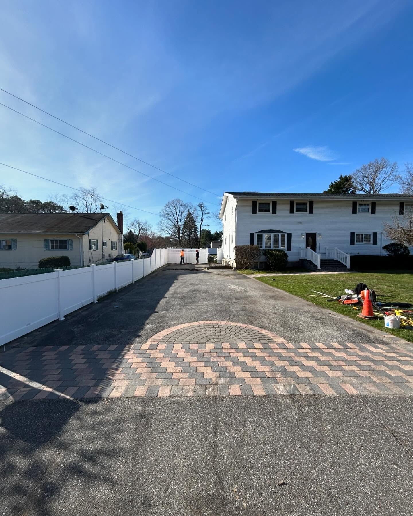 A brick driveway leading to a house with a white fence.