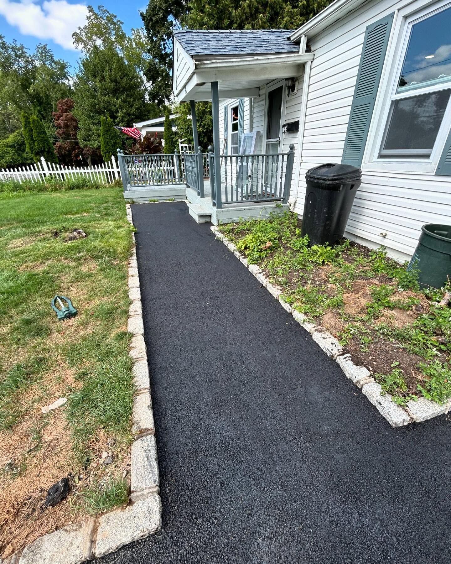 A black walkway leading to a white house with a porch.