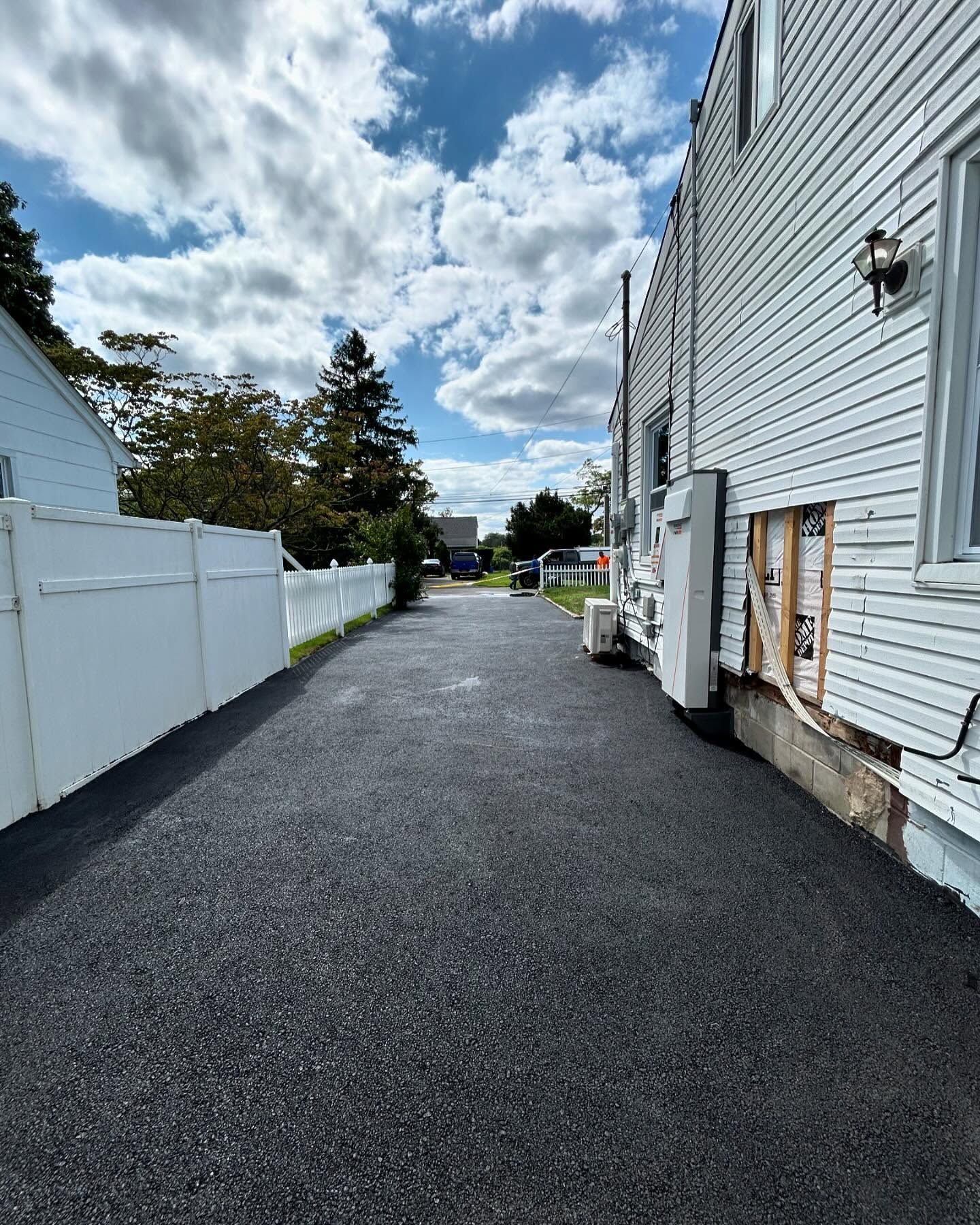 A driveway leading to a white house with a white fence.