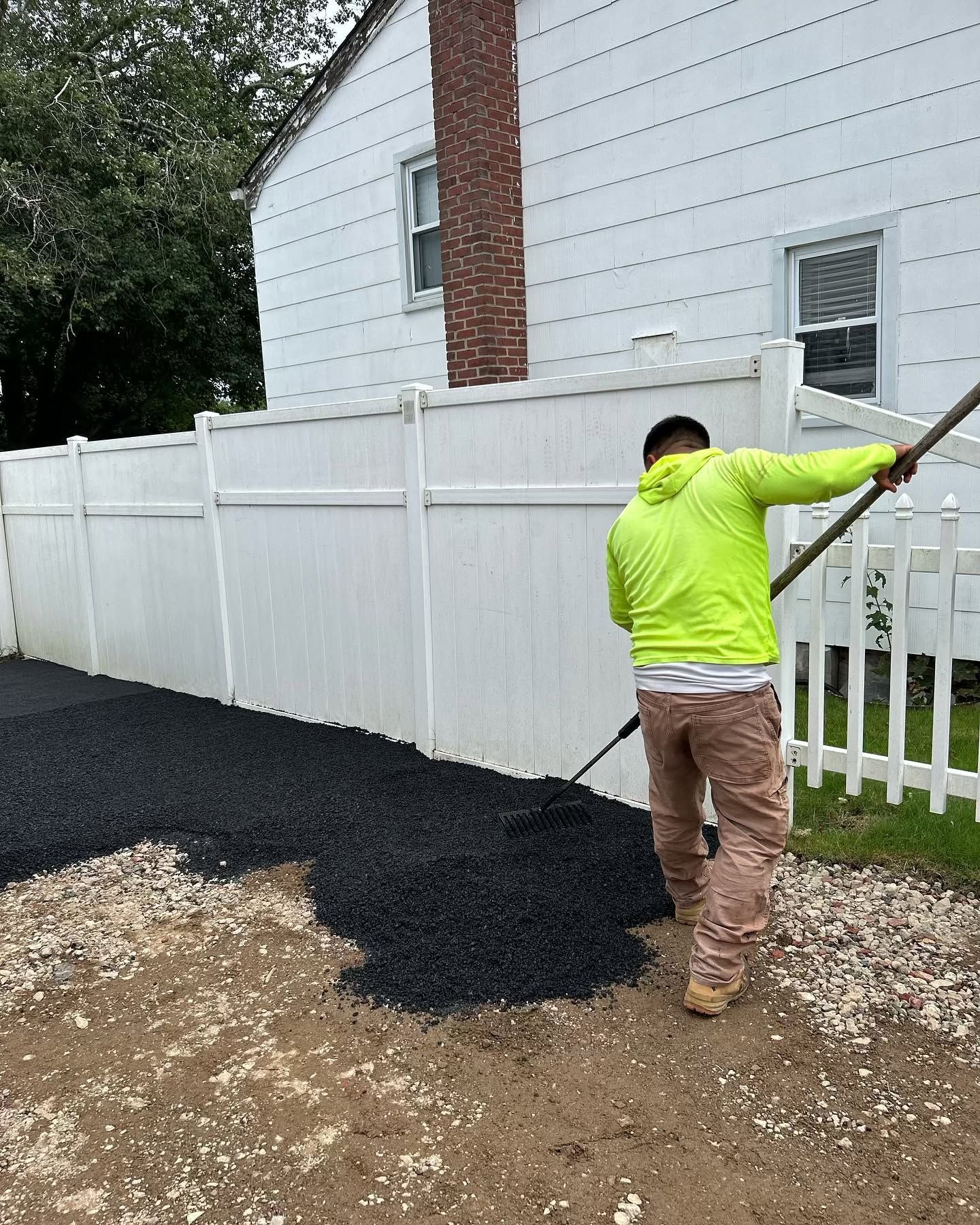 A man is raking gravel in front of a white fence.