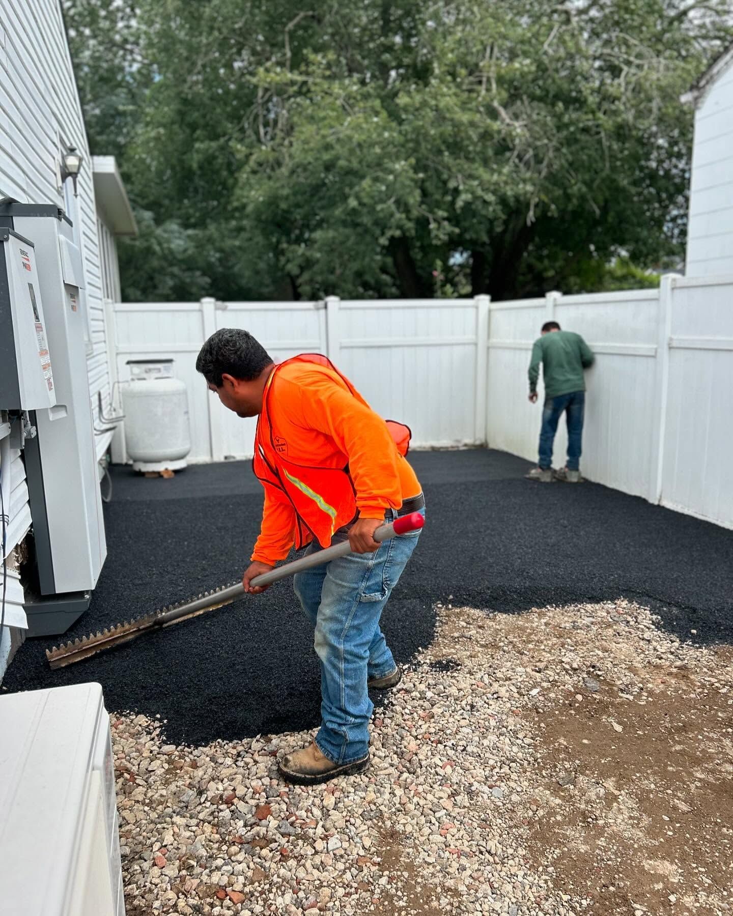 A man is raking gravel in a backyard with a broom.