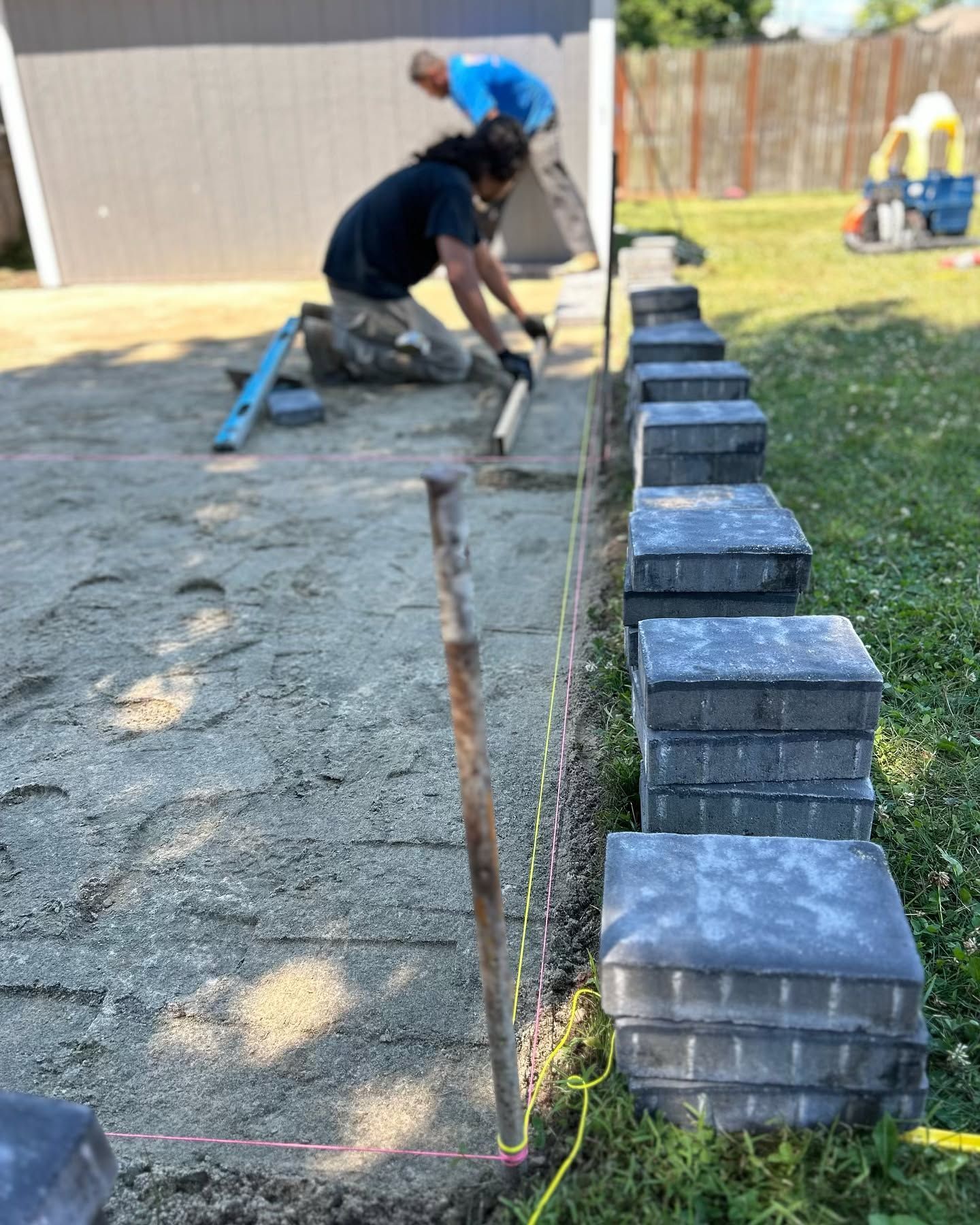 Two men are working on a patio in a backyard.