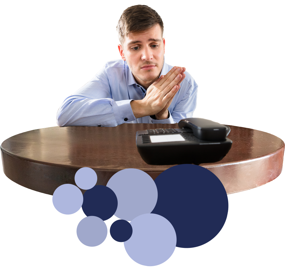 Een man zit aan een tafel met zijn handen gevouwen voor een telefoon