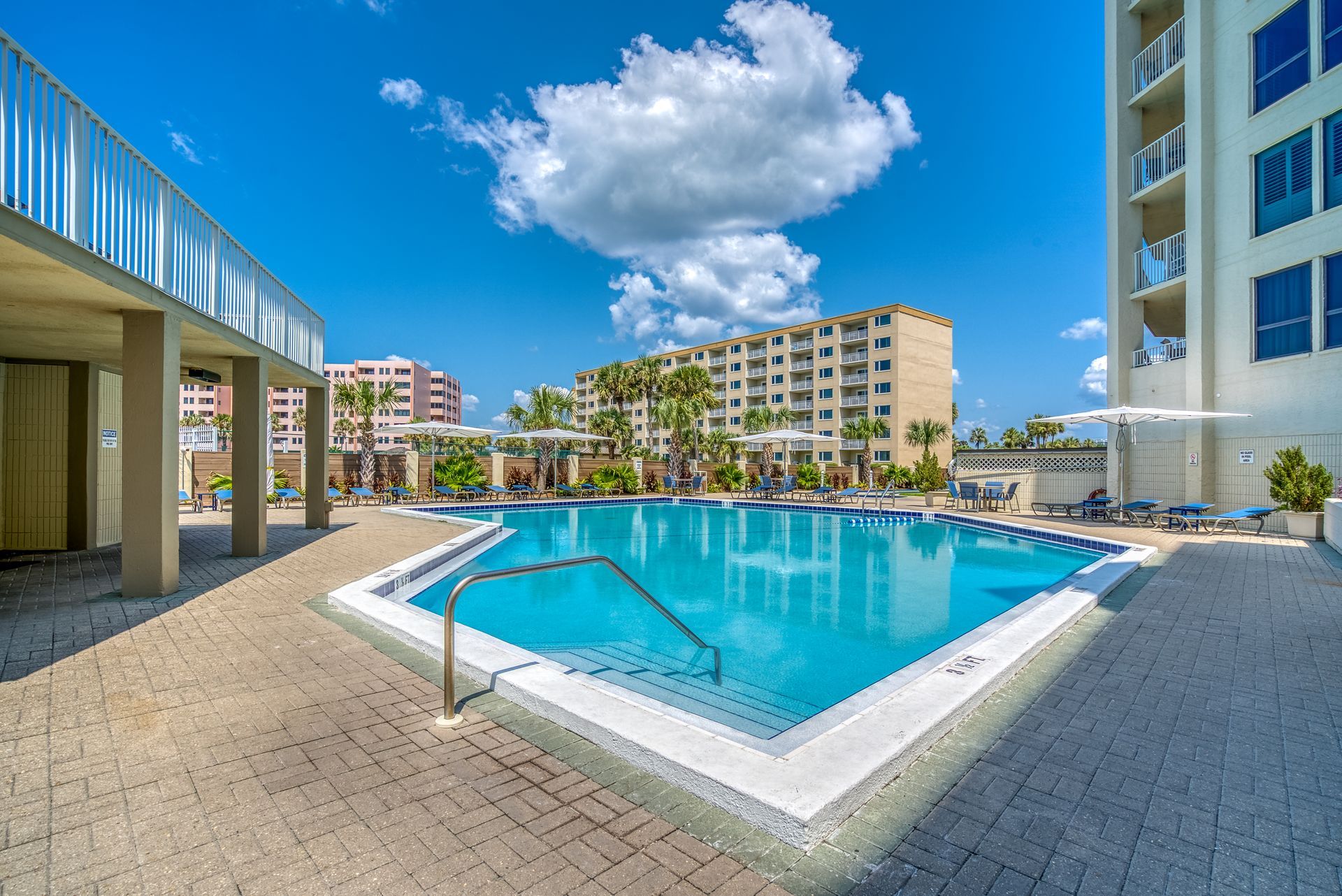 A large swimming pool surrounded by chairs and umbrellas in front of a building.