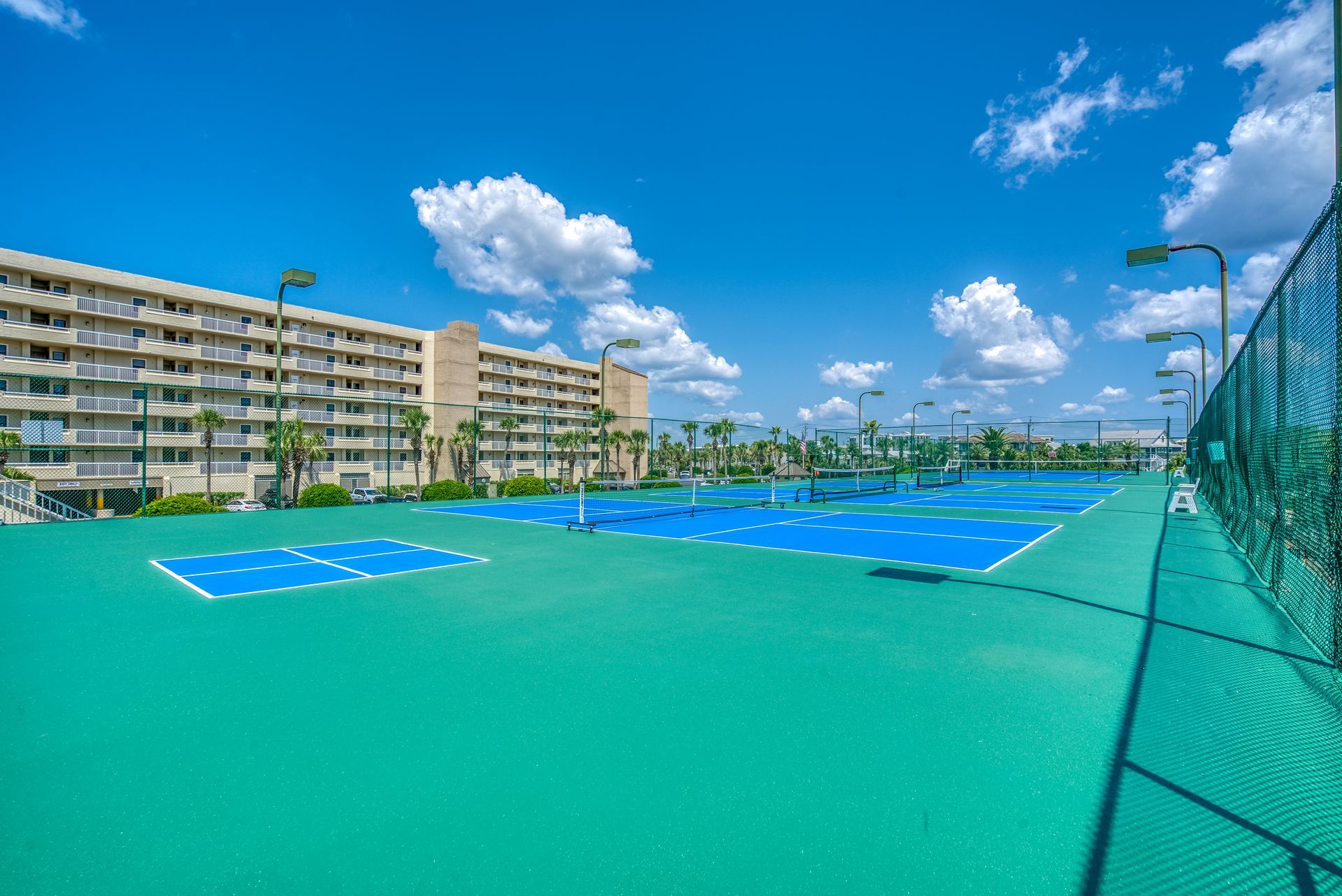 A tennis court with a fence and a building in the background.