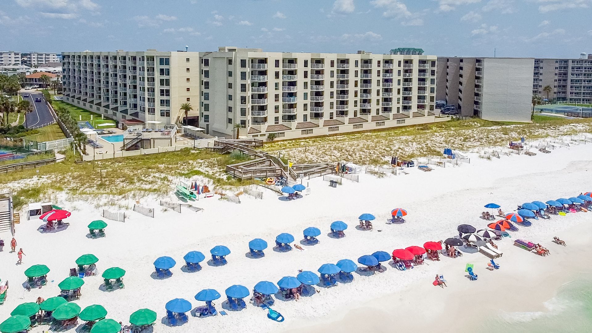 An aerial view of a beach with umbrellas and chairs and a large building in the background.