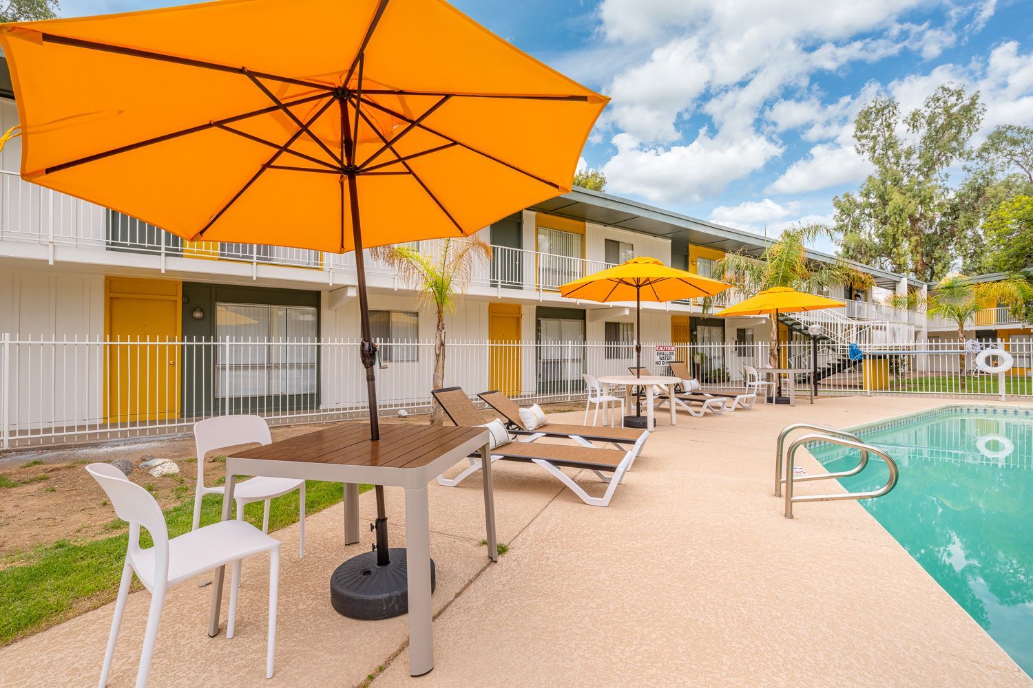 a yellow umbrella sits in front of a swimming pool