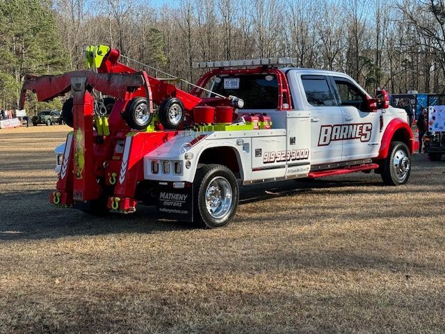 White and red tow truck with boom on grassy field.