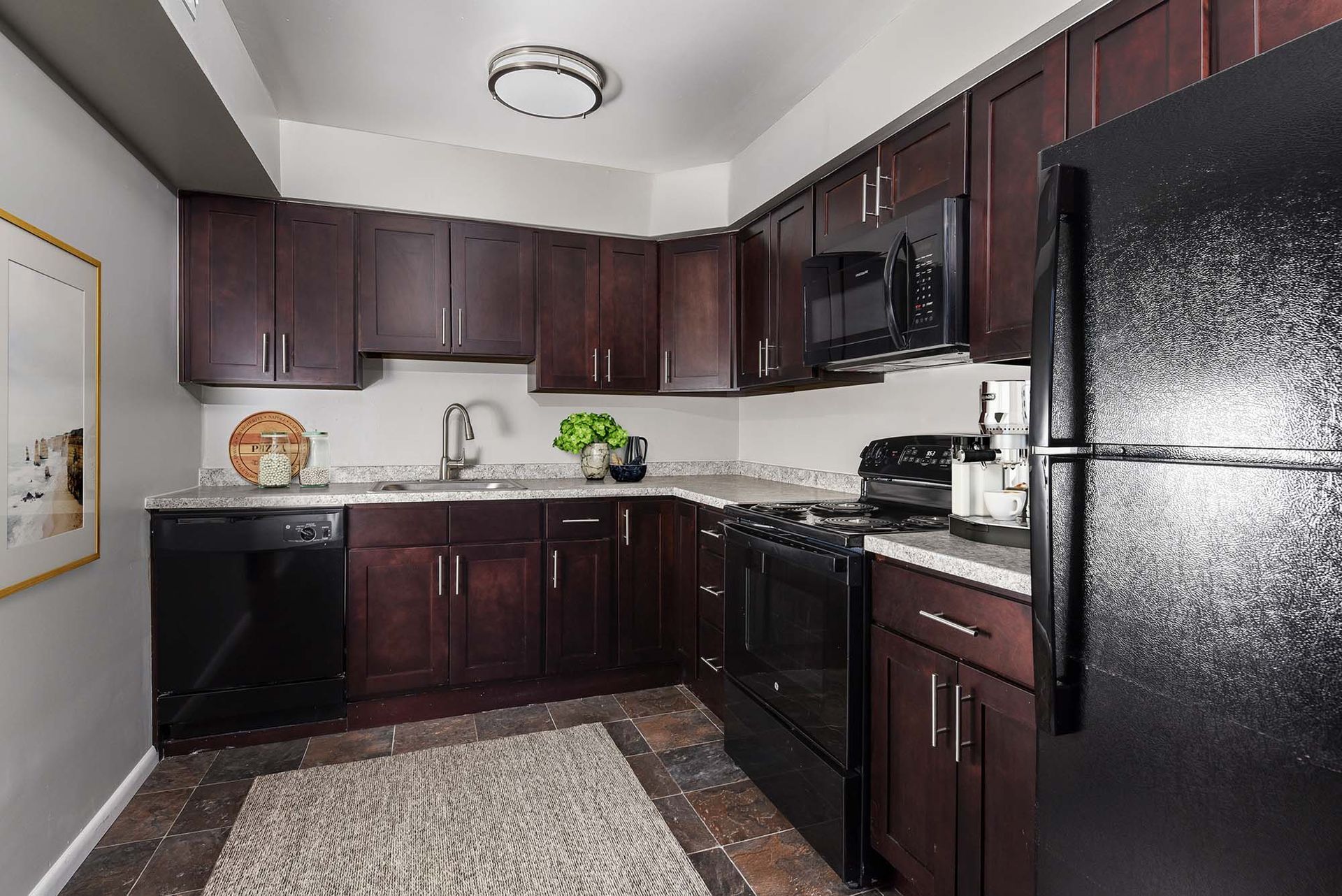 U-shaped kitchen with dark wood cabinets, black appliances, and a granite-style countertop.