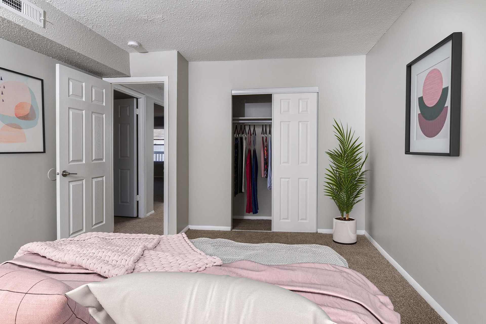 Bedroom with bed in foreground, open closet with clothes, and a potted plant.