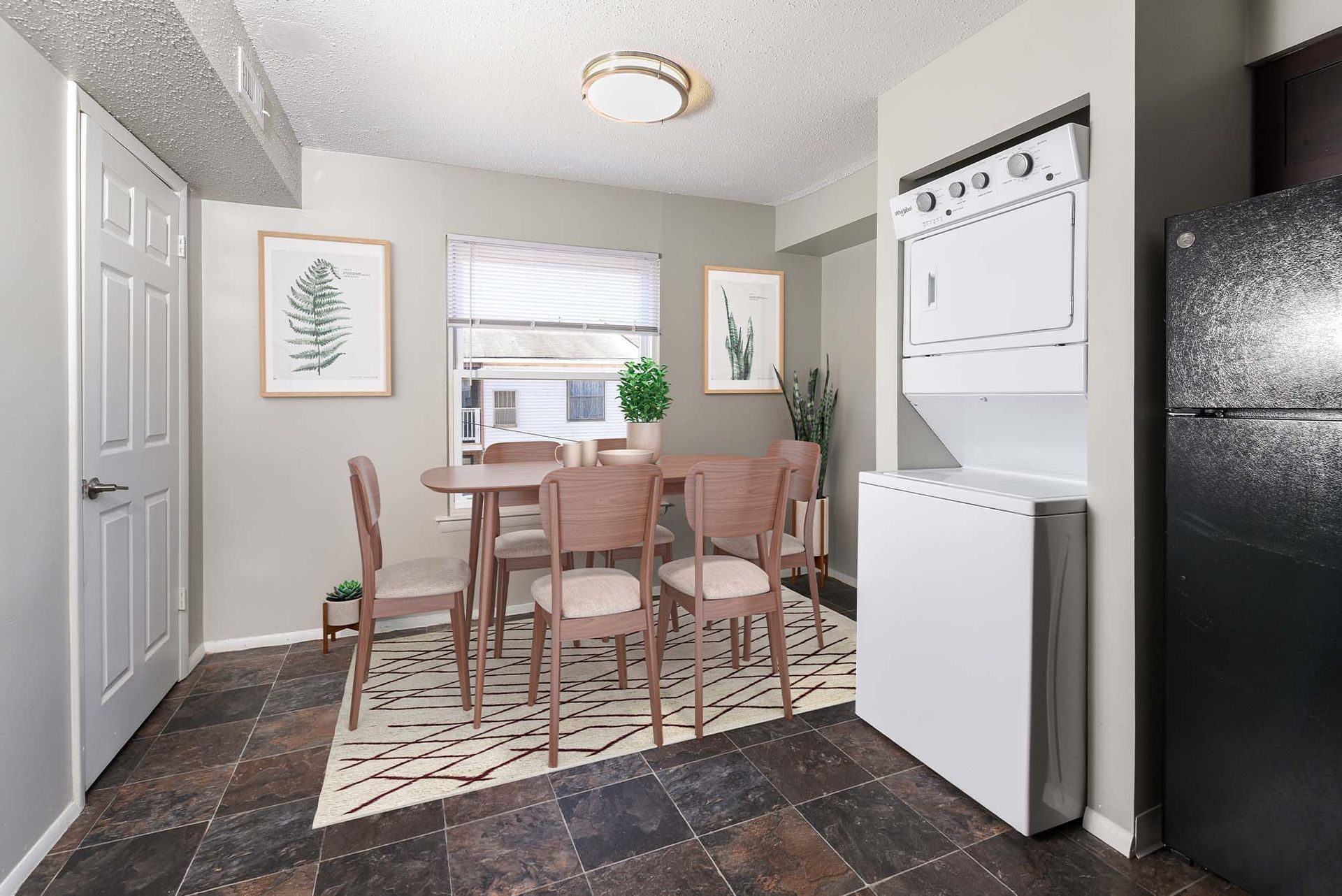 Apartment dining area with wooden table and six chairs beside a stacked washer/dryer and fridge.
