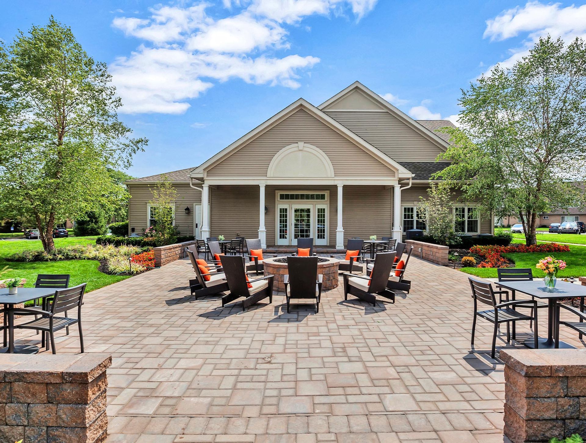 Outdoor communal patio with a circular fire pit and lounge chairs in front of a clubhouse.