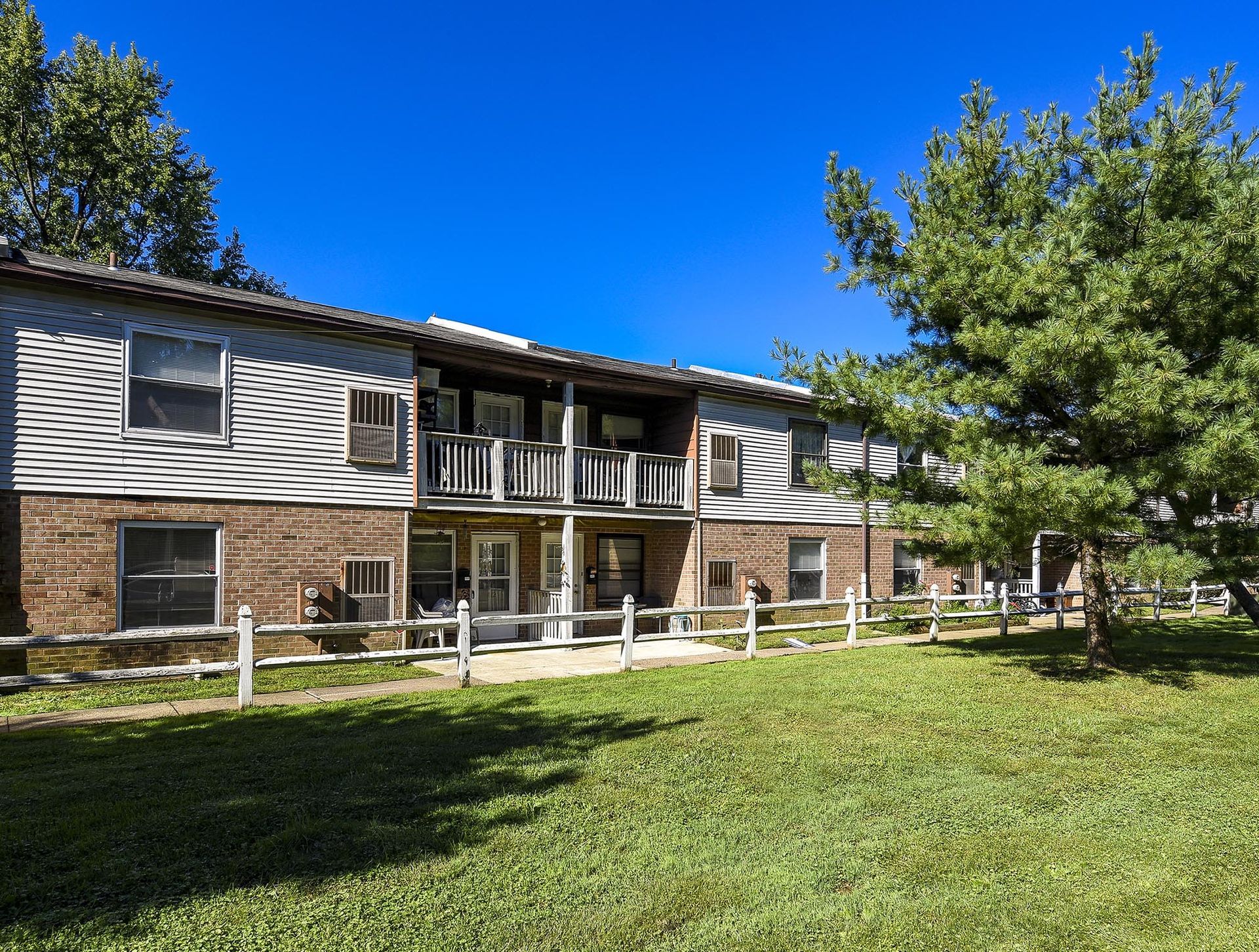 Exterior view of a two-story apartment building with a balcony and a grassy lawn.