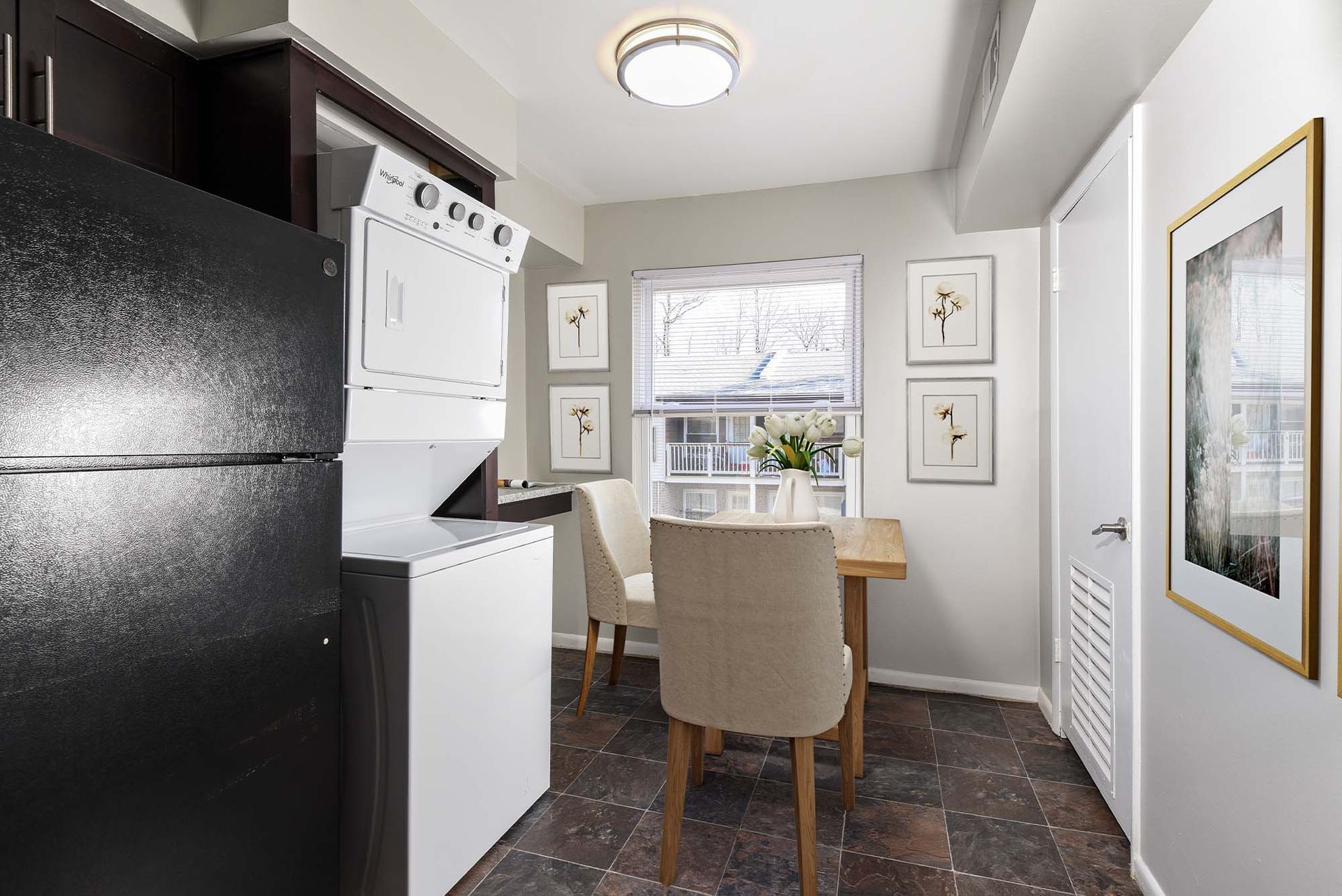 Small apartment dining area with a stacked washer/dryer on the left, wooden table, and beige chairs.