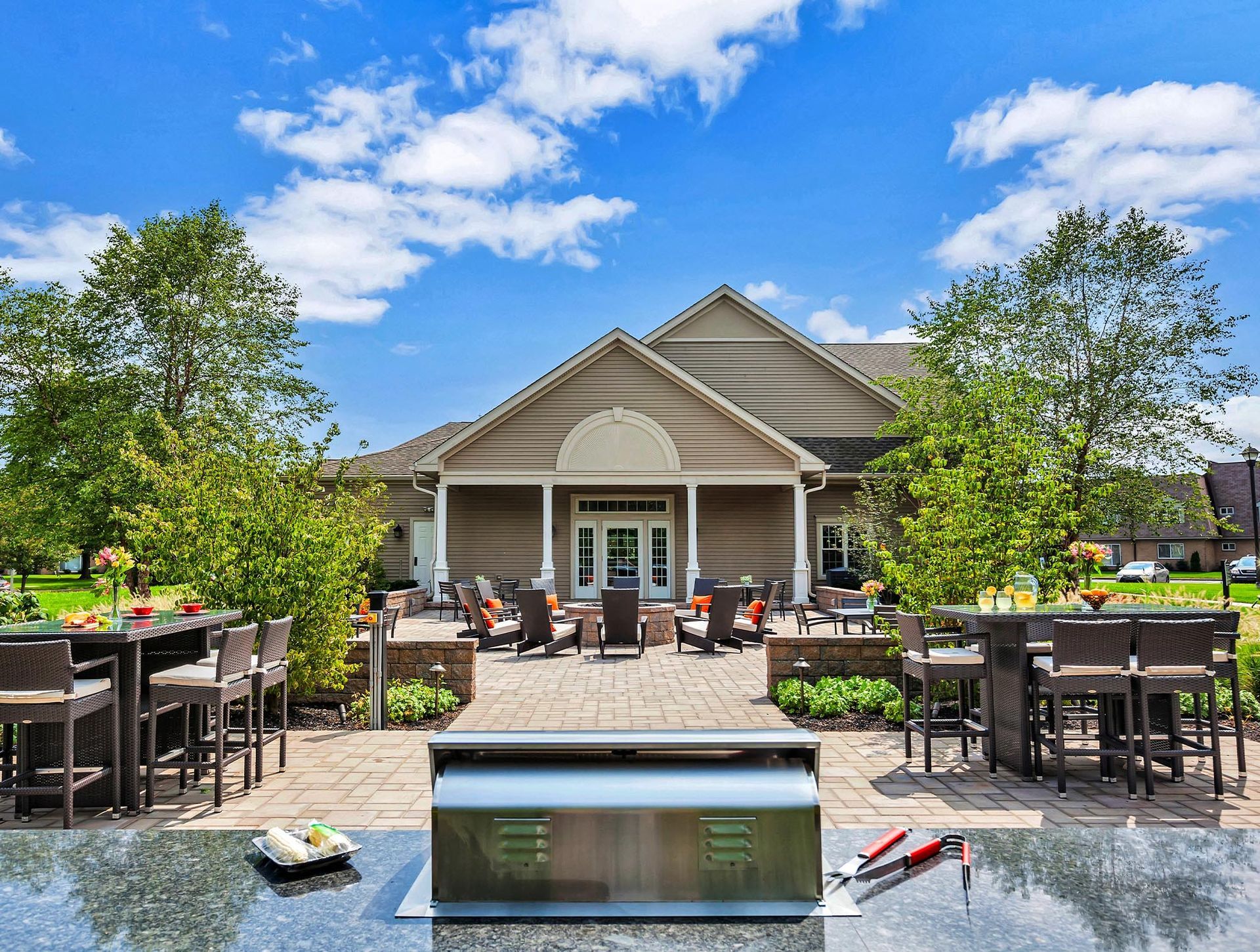 Outdoor communal patio with grill, tables, and seating near a clubhouse.