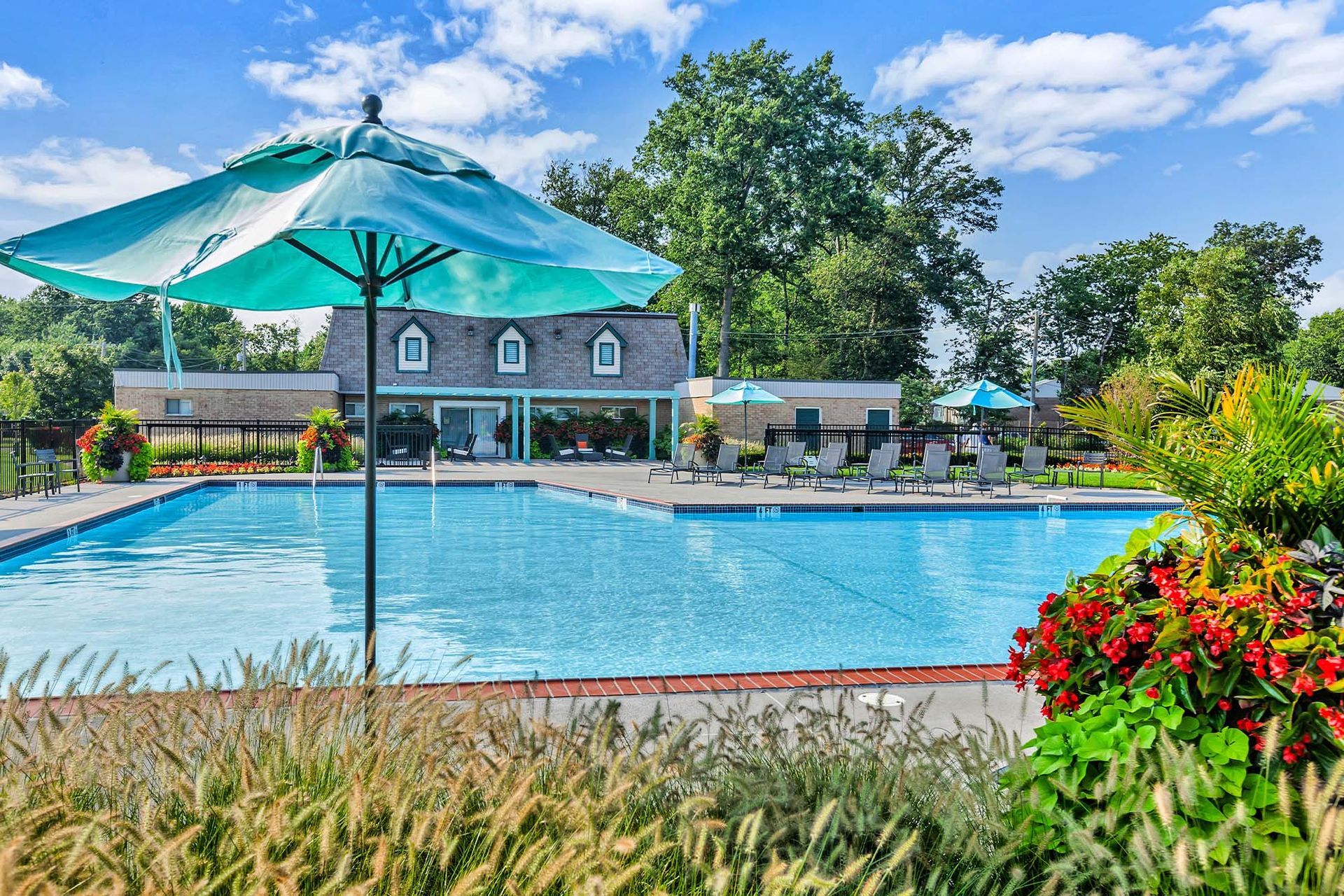 Outdoor community pool with lounge chairs, umbrellas, and landscaped surroundings.