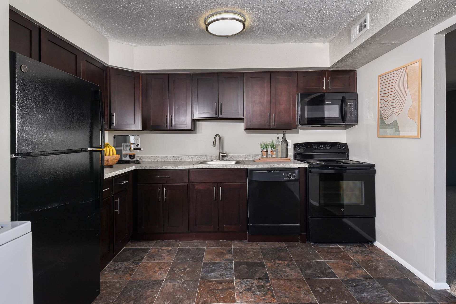 Apartment kitchen with dark wood cabinets, black appliances, and granite countertops.