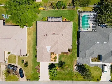 Overhead view of a house with a driveway, lawn, and pool. Two cars parked on the property.