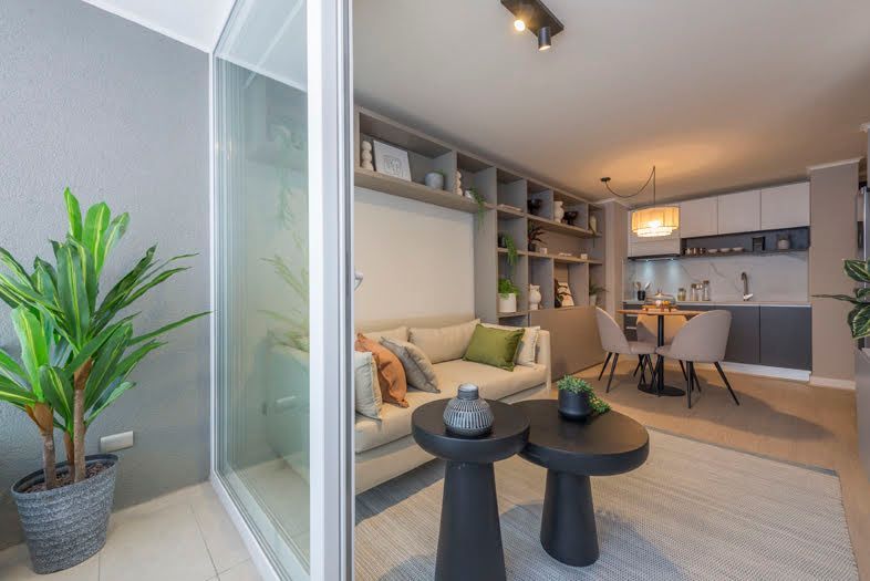 Moderna sala de estar con sofá, estanterías y cocina visibles a través de una pared de vidrio.