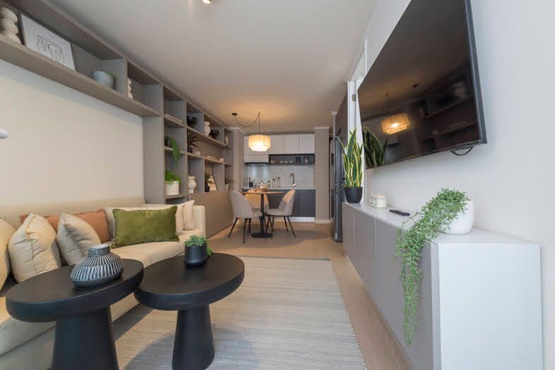 Sala de estar con sofá, mesas de centro, TV, estanterías empotradas y un comedor visible al fondo.